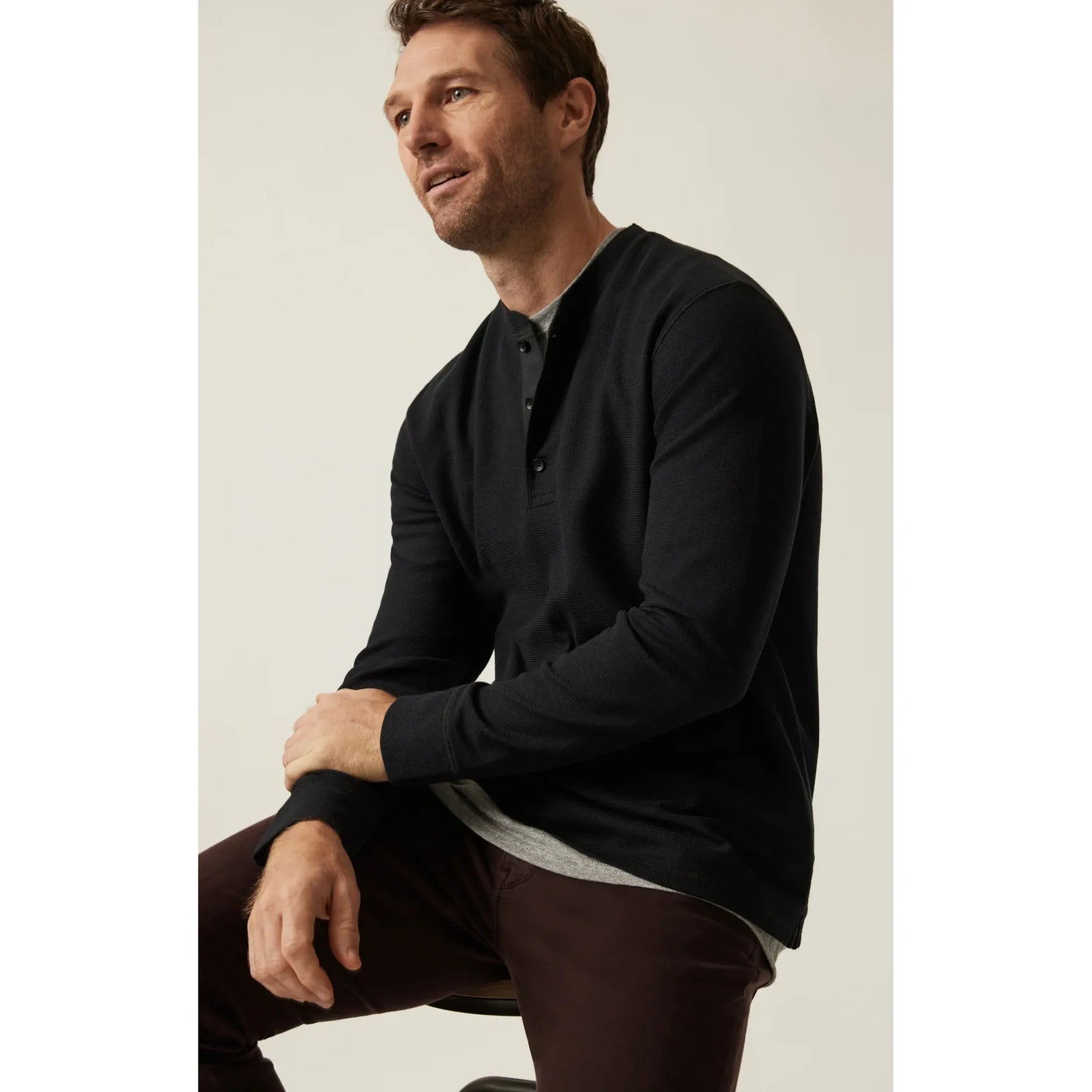 Man wearing black 34 Heritage Long Sleeve Henley with button placket, seated.