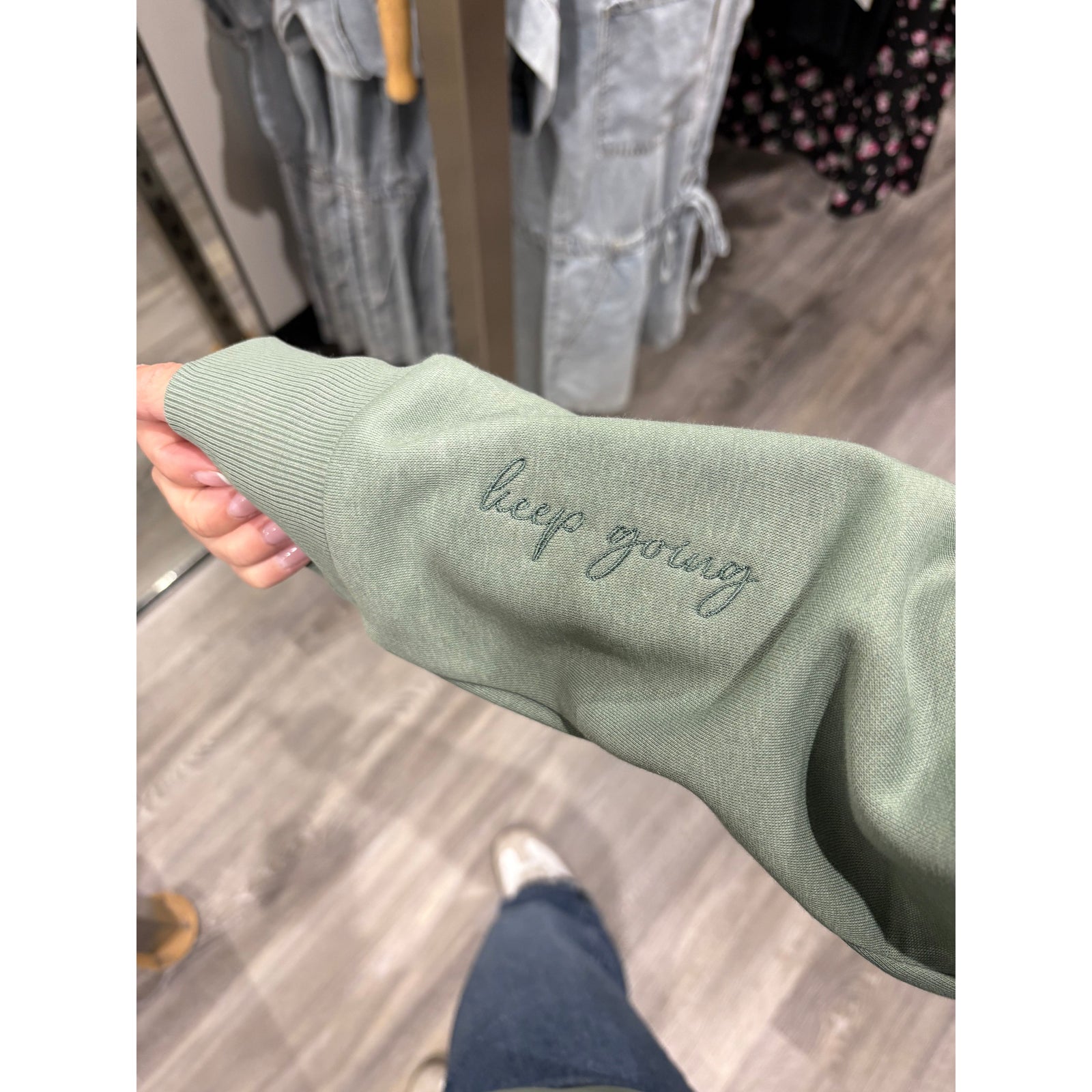 Keep Going Half Zip Hoodie sleeve with embroidered 'keep going' on a sage green hoodie.