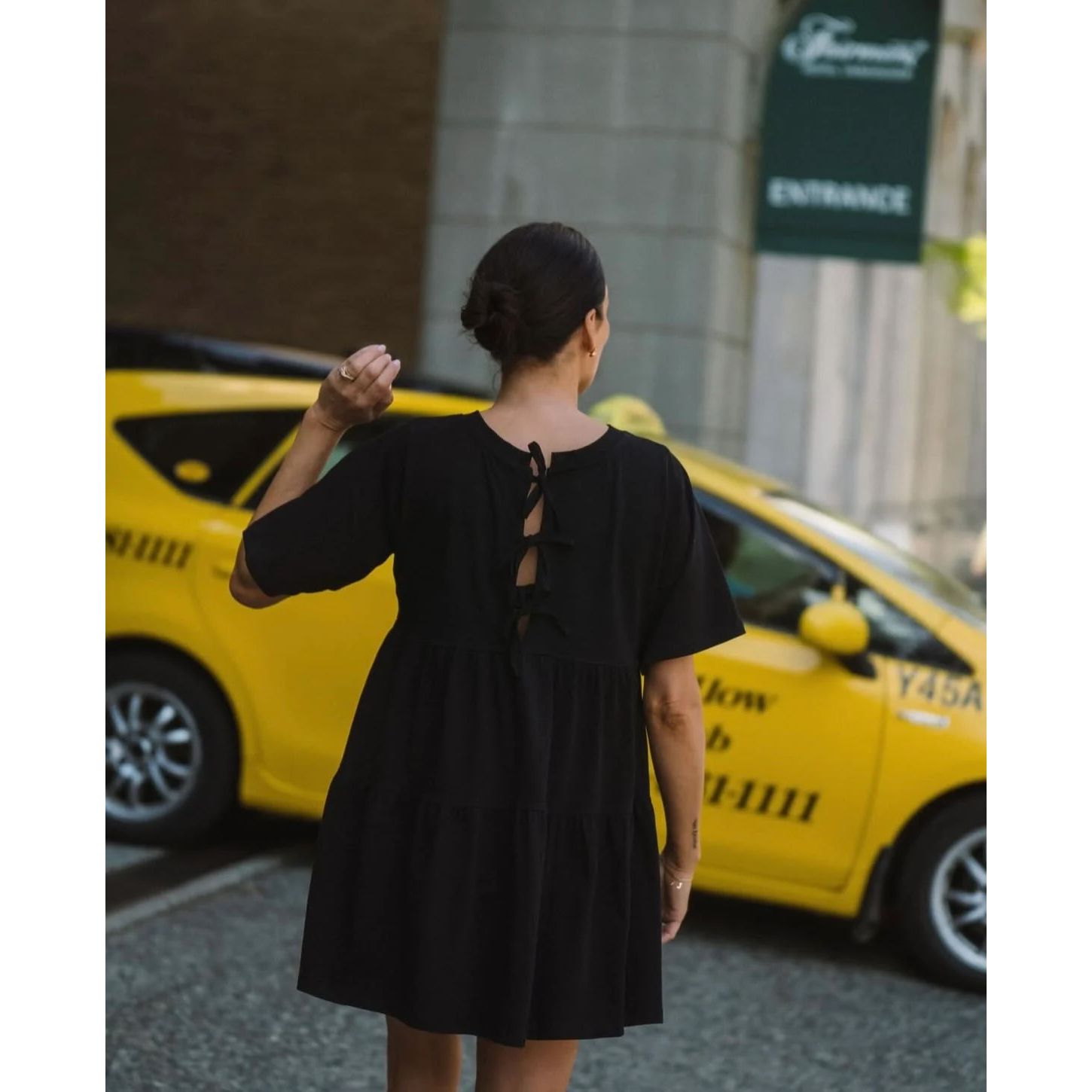 Woman wearing Brunette The Label Tiered Dress in black cotton with back three-bow ties and an oversized fit.