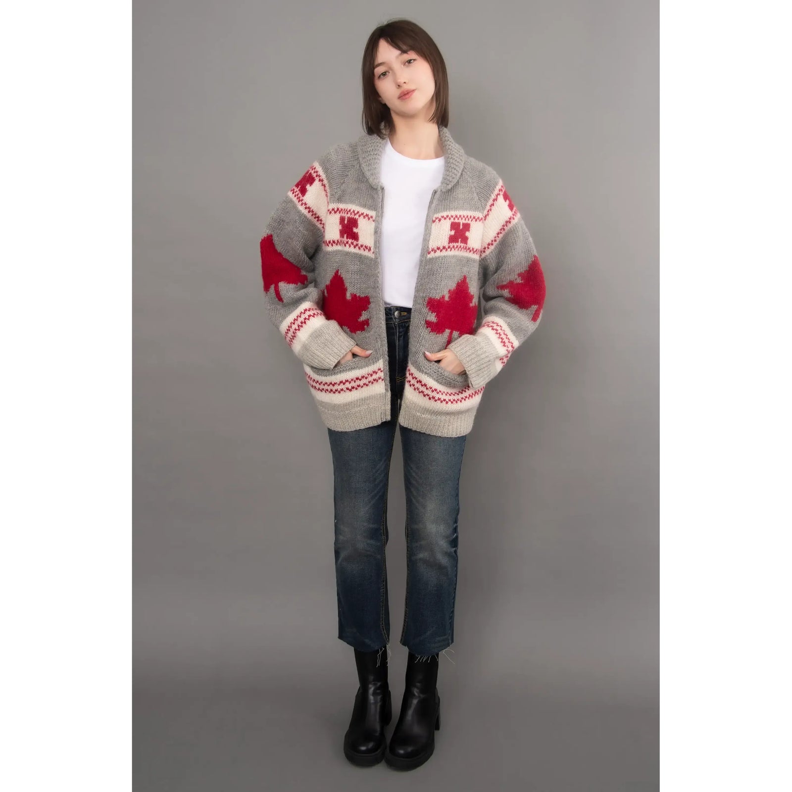 Gray knit cardigan with red maple leaf pattern, shawl collar, and raglan sleeves styled with blue jeans and black boots.