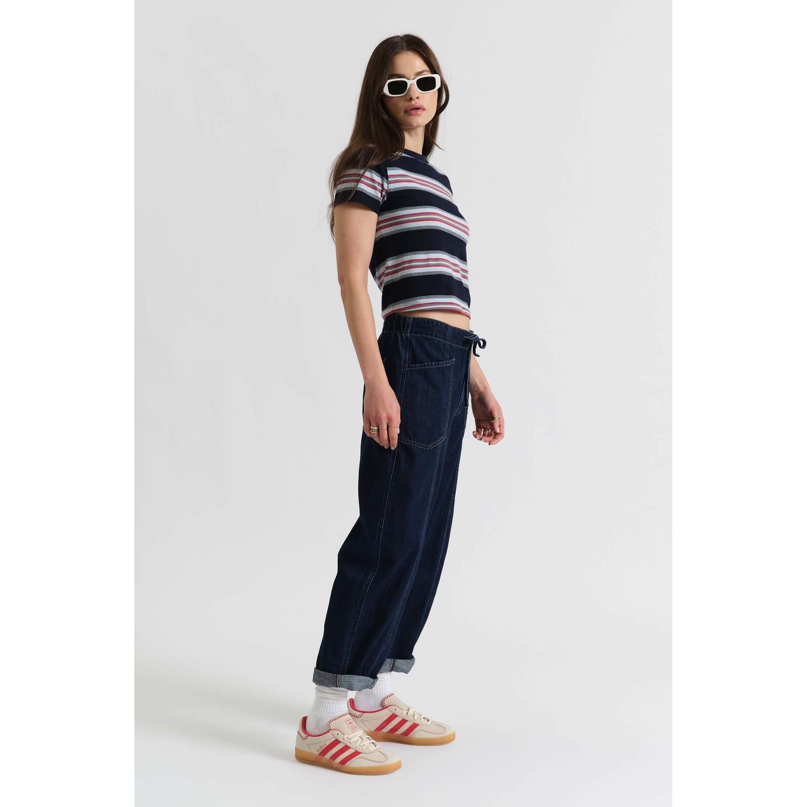 Model wearing Daze Villa Drawstring Barrel in Blue Mood pants with a striped crop tee, sunglasses, and sneakers.