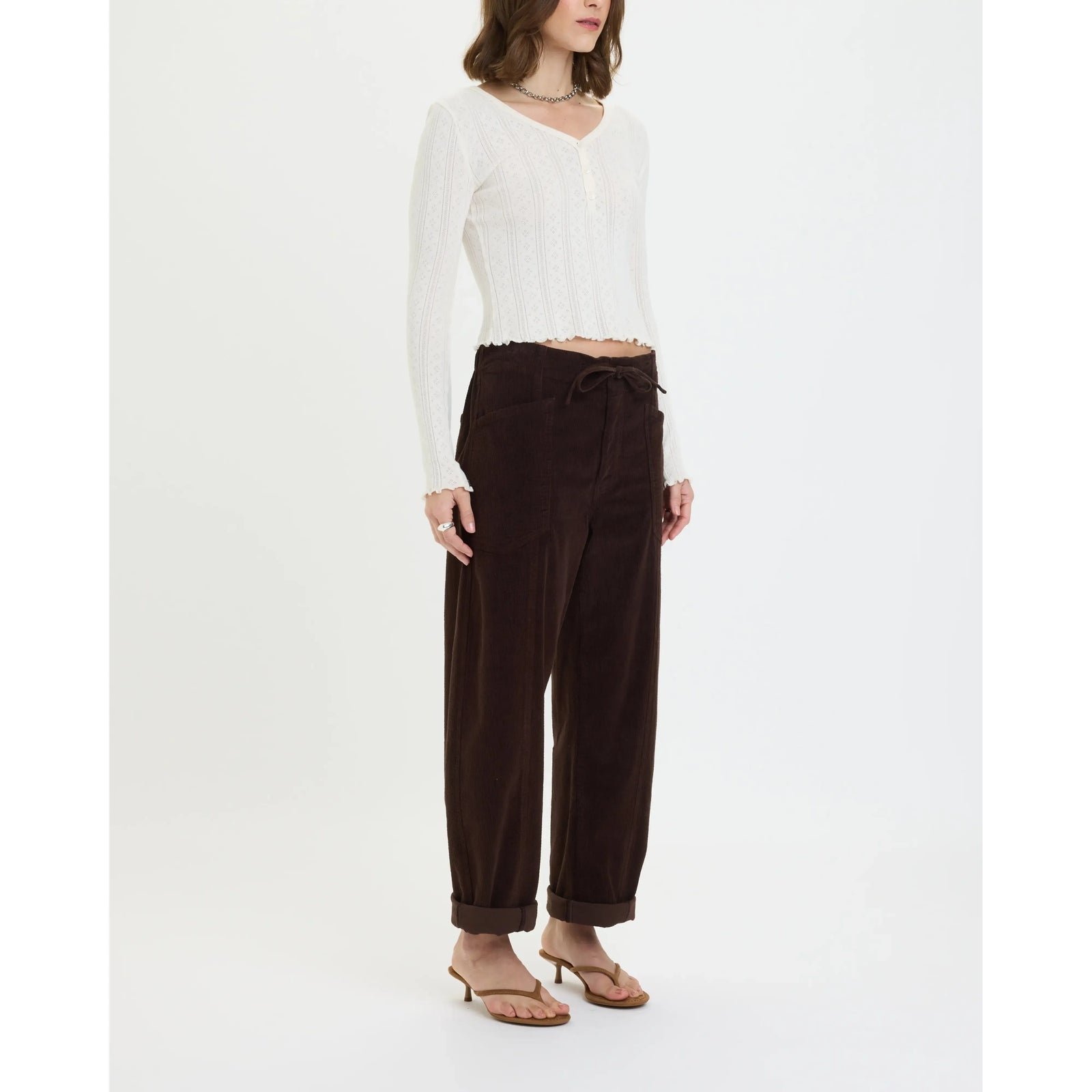 Model wears chocolate brown corduroy drawstring barrel pants with side pockets and cuffed ankles, styled with a white cropped top.