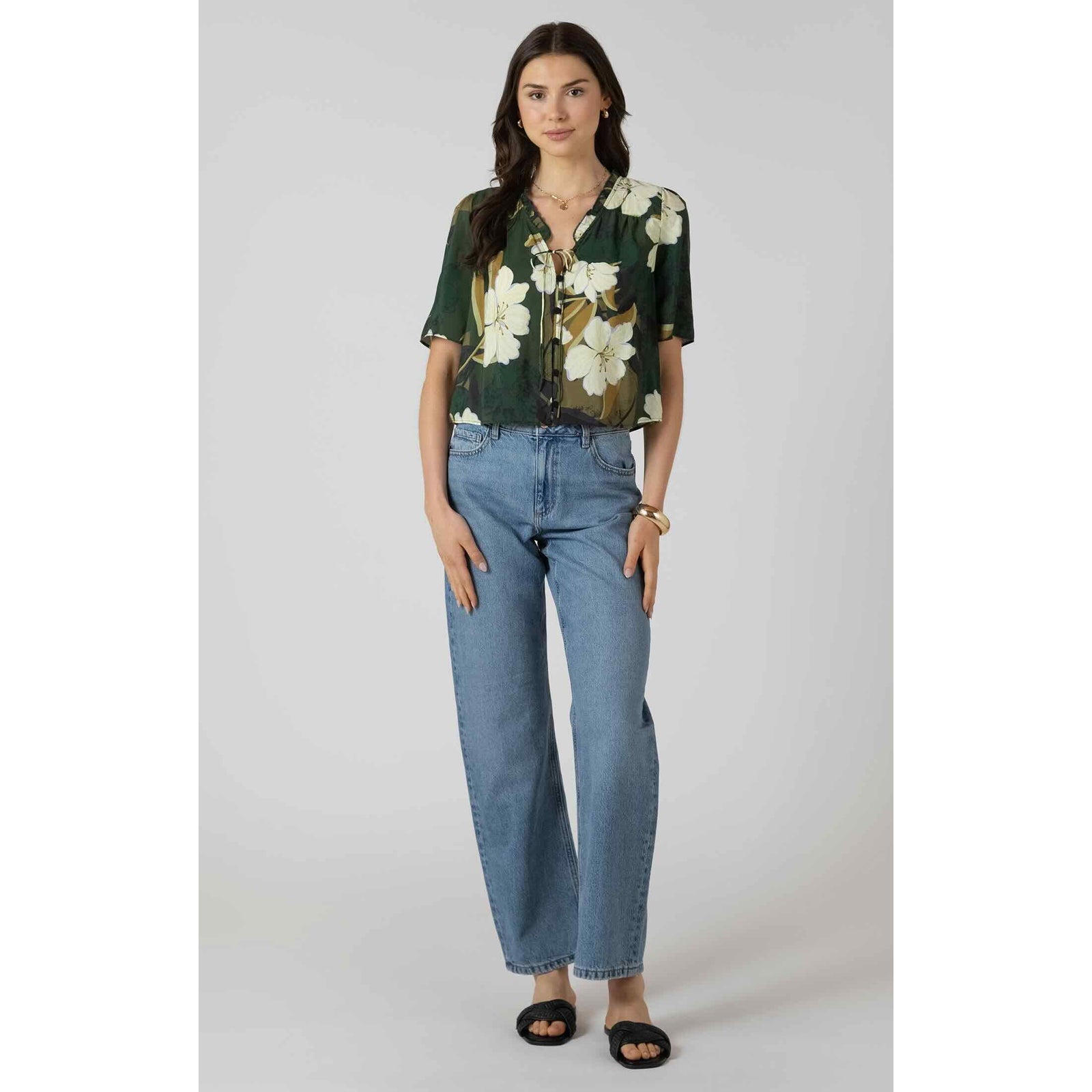 Model wearing Dex Button Front Ruffle Trim Blouse in green floral print with button-front and ruffle trim, blue jeans.