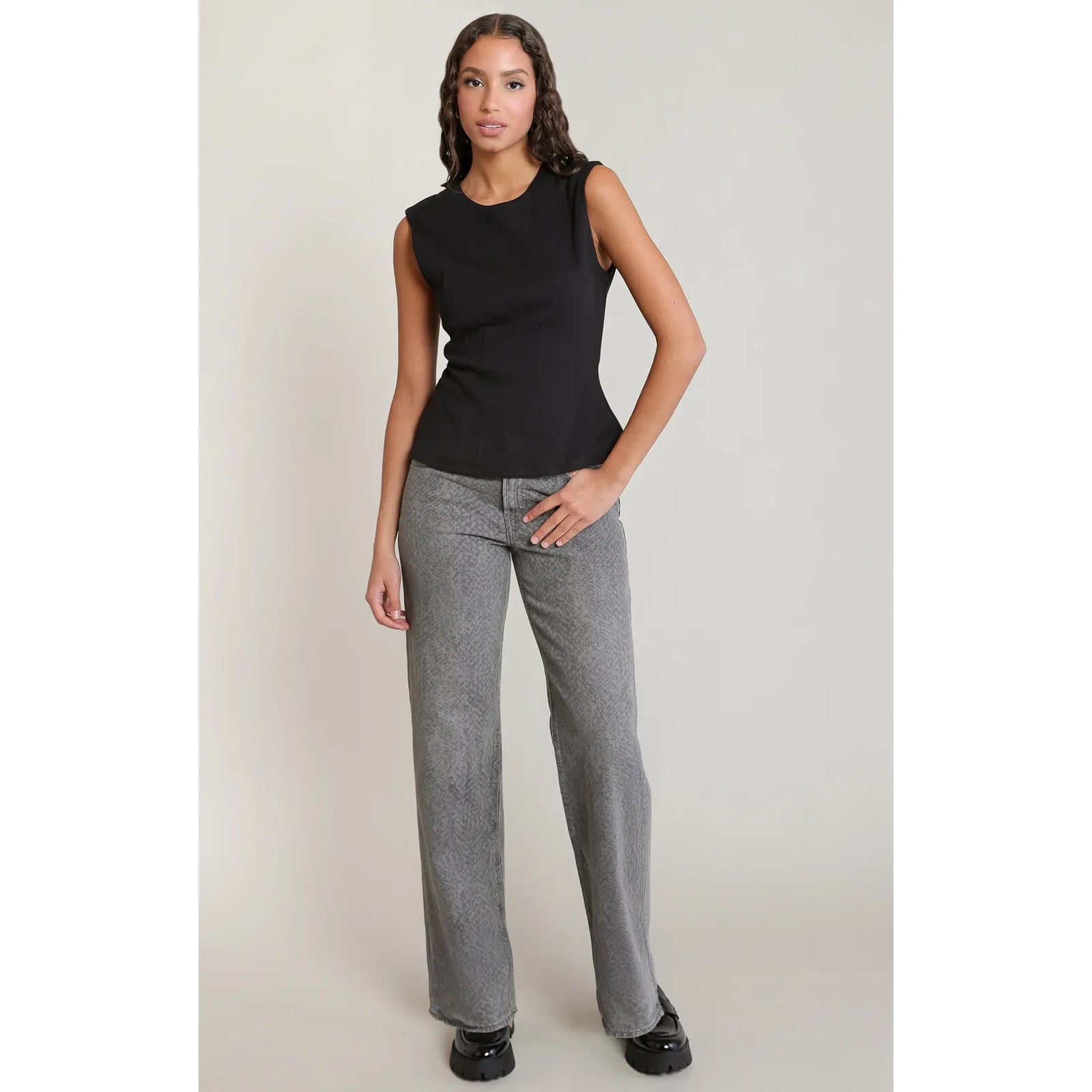 Black sleeveless cinch waist top with a scoop neck, paired with grey wide-leg pants and black platform shoes.