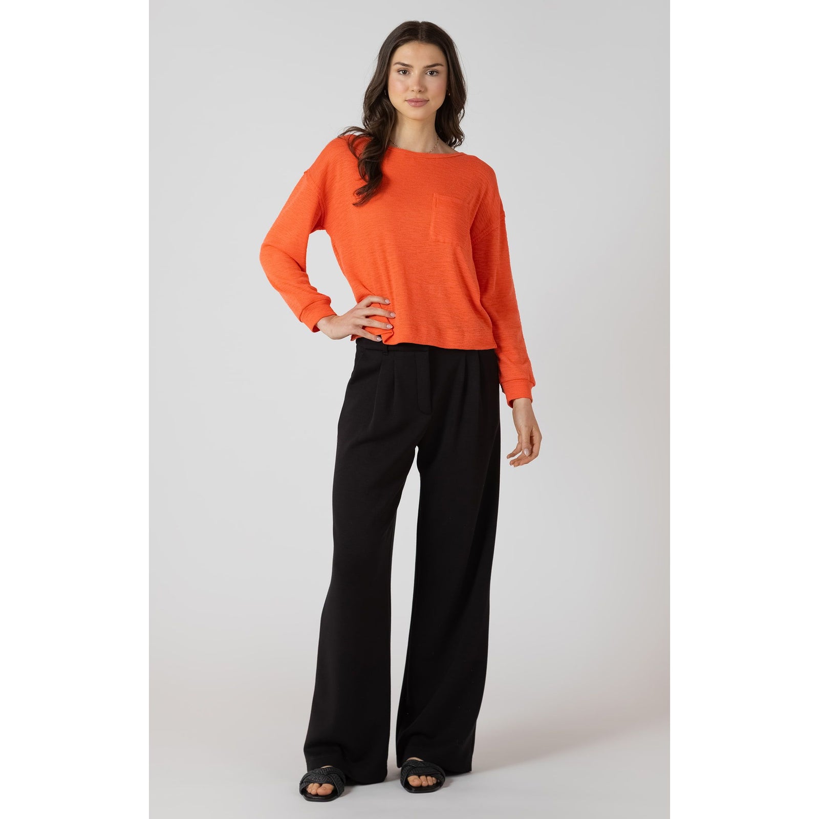 Dex Crewneck Sweatshirt in bright orange with chest pocket on model, paired with black wide-leg pants.