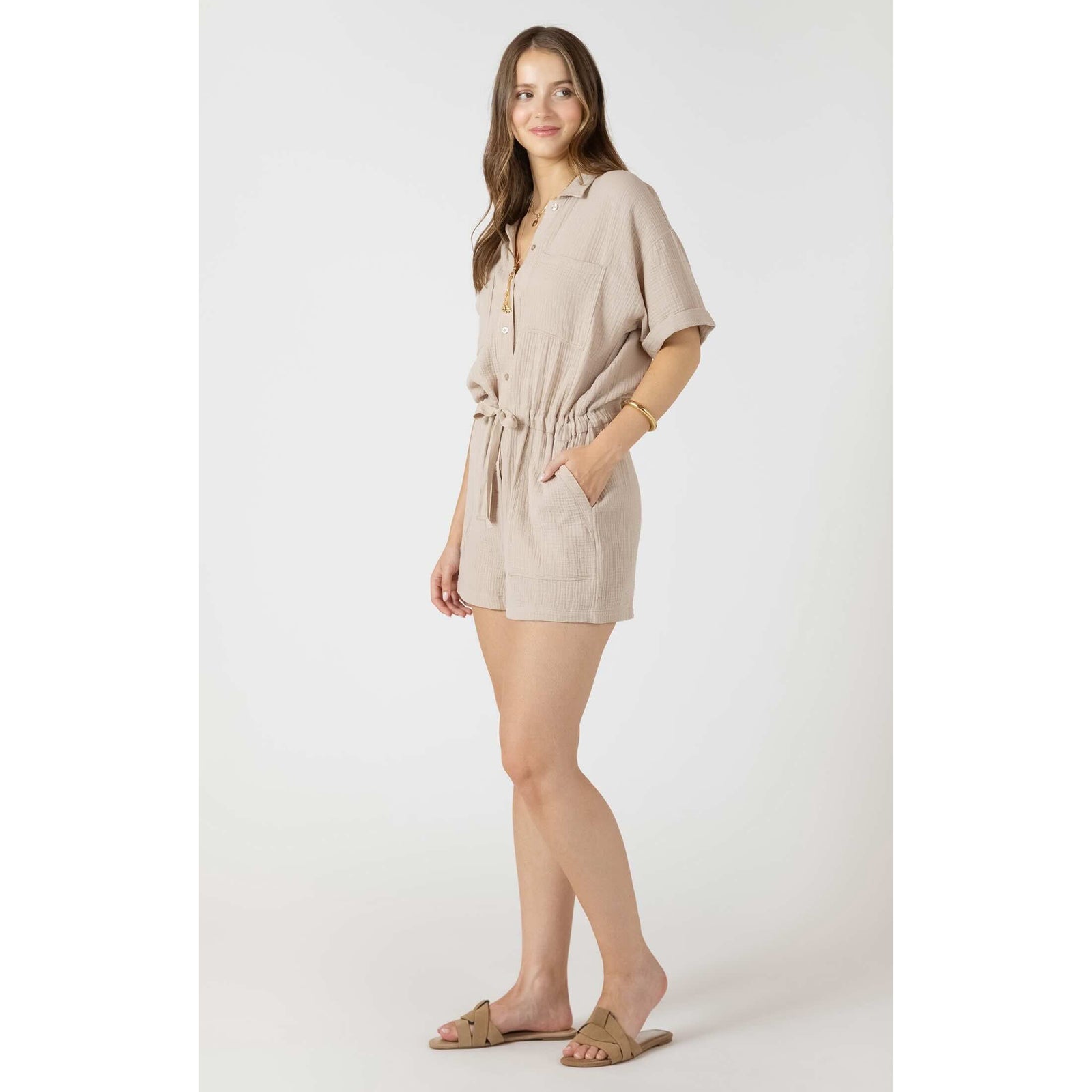 Dex Polo V-Neck Romper on a model with rolled sleeves, drawstring waist and pockets, paired with tan sandals.