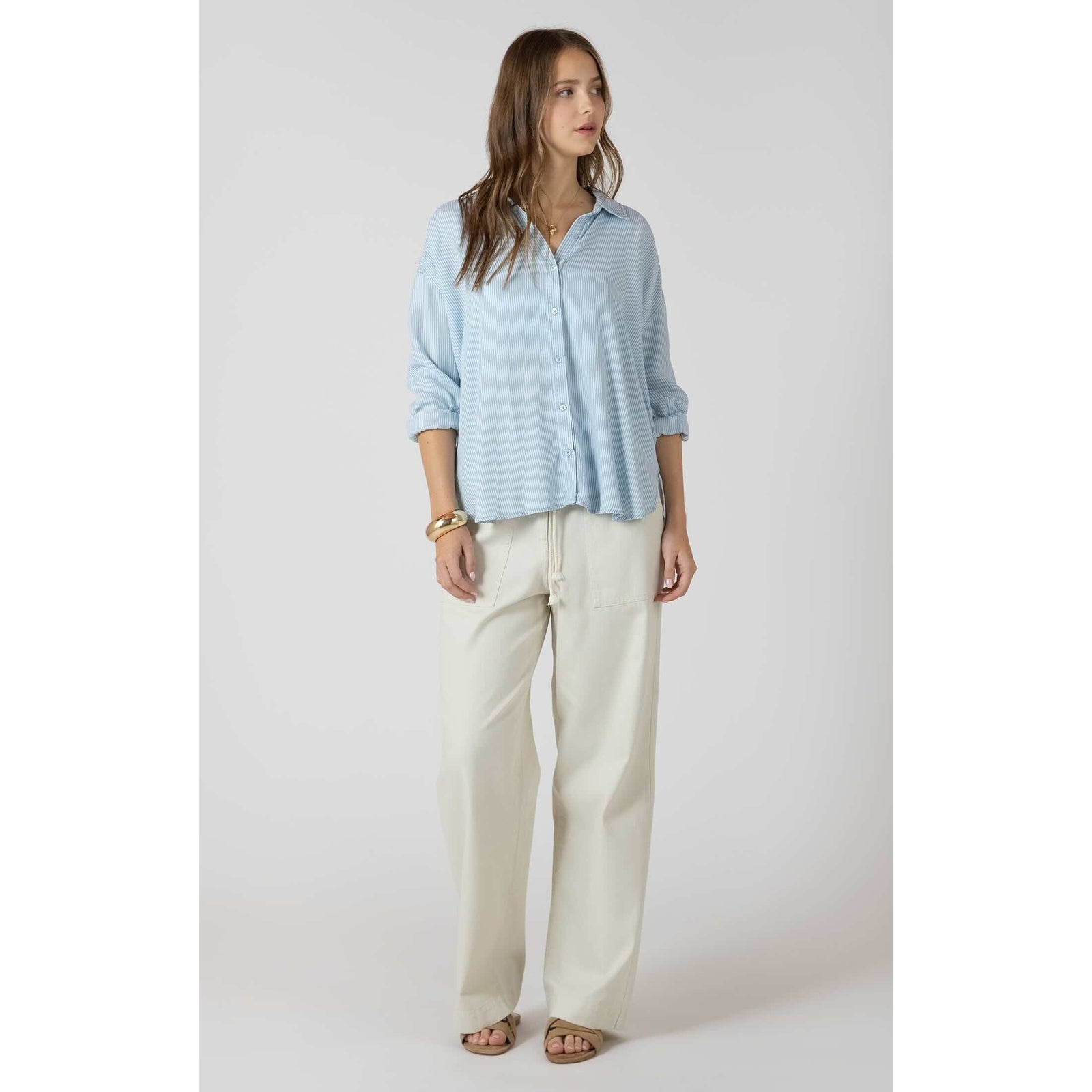 Dex Relaxed Button Front Shirt in light blue stripes, relaxed fit, rolled sleeves, paired with ivory pants.