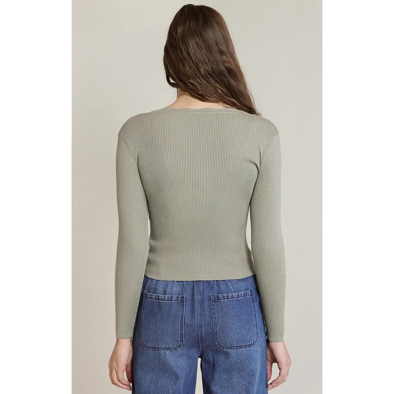 Back view of a sage green long-sleeve ribbed knit top with a scalloped neckline paired with blue denim jeans.