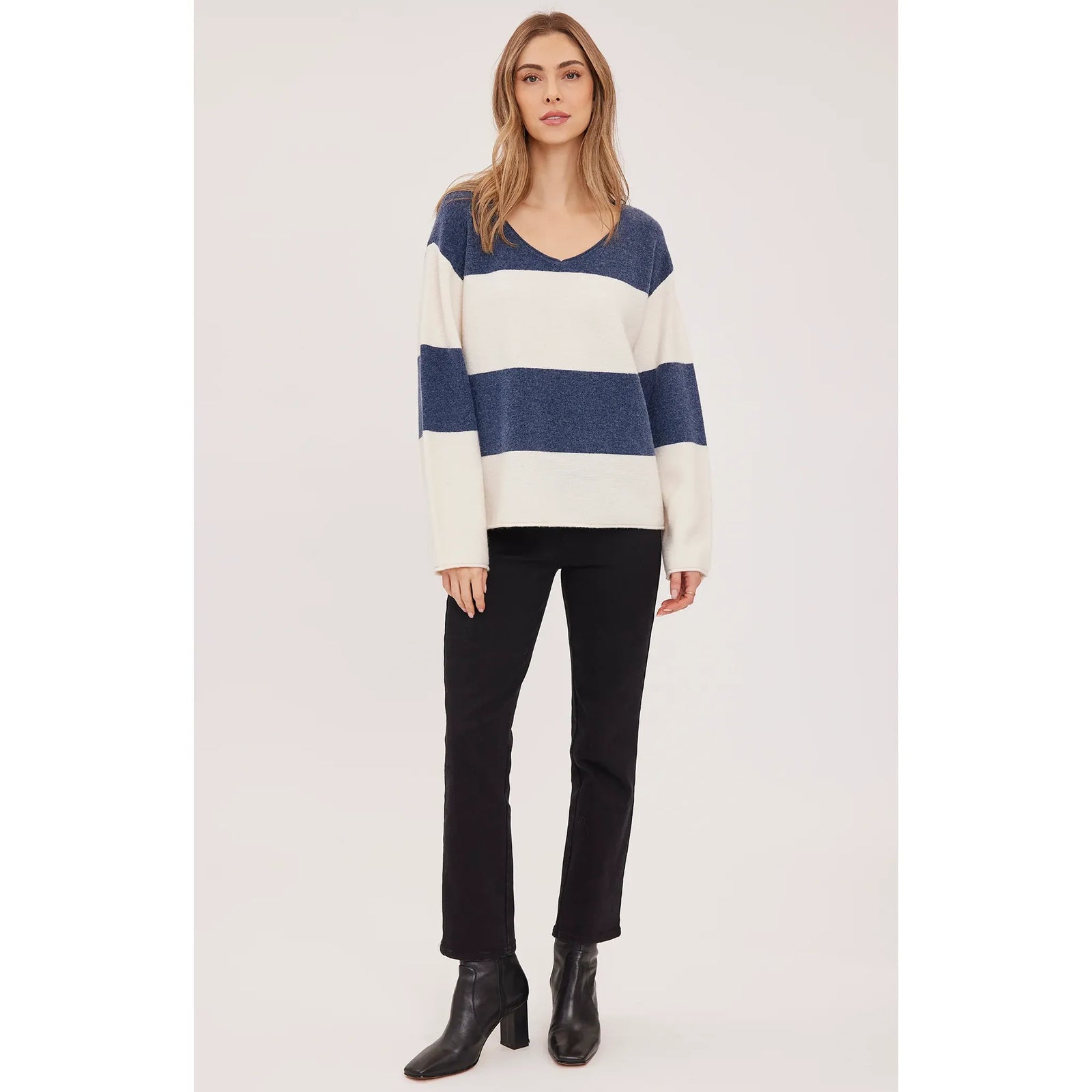 Oversized V-neck sweater in blue and cream stripes with soft textured knit, rolled edges, and relaxed fit paired with black boots.