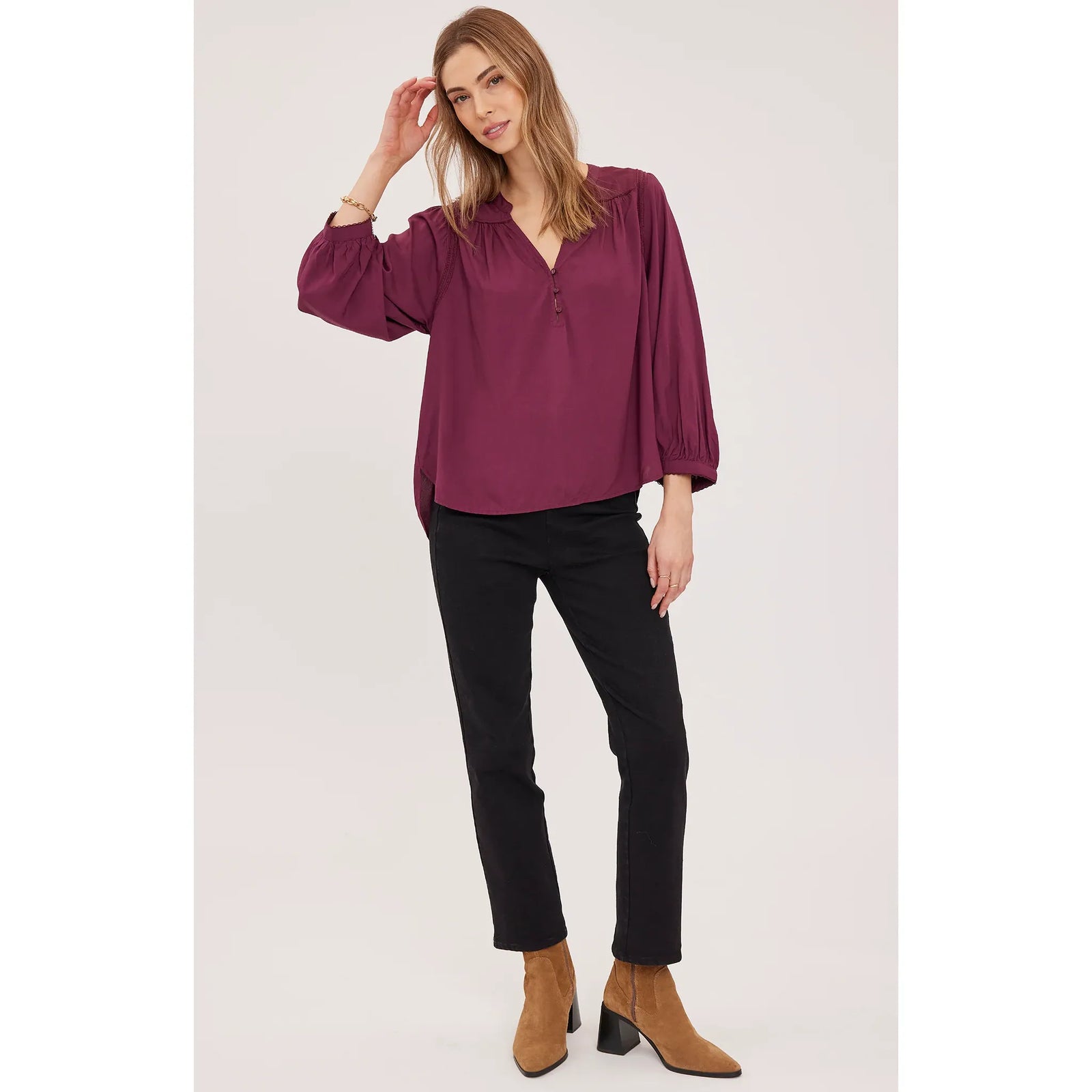 Model wearing a plum viscose Ashlyn blouse with balloon sleeves and lace trim, paired with black pants and tan block-heeled boots.