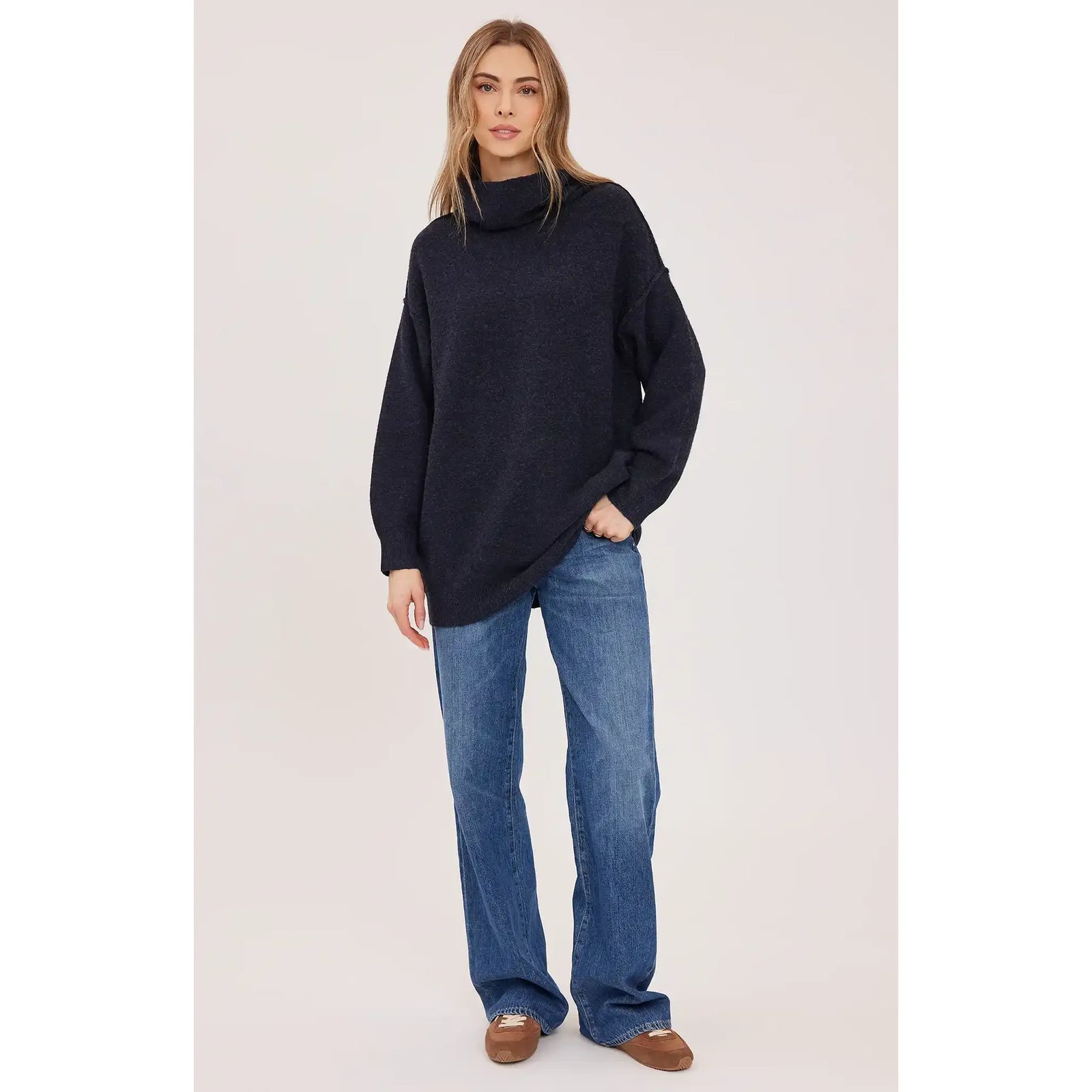 Model wearing an oversized dark textured turtleneck sweater with wide-leg jeans and brown loafers.