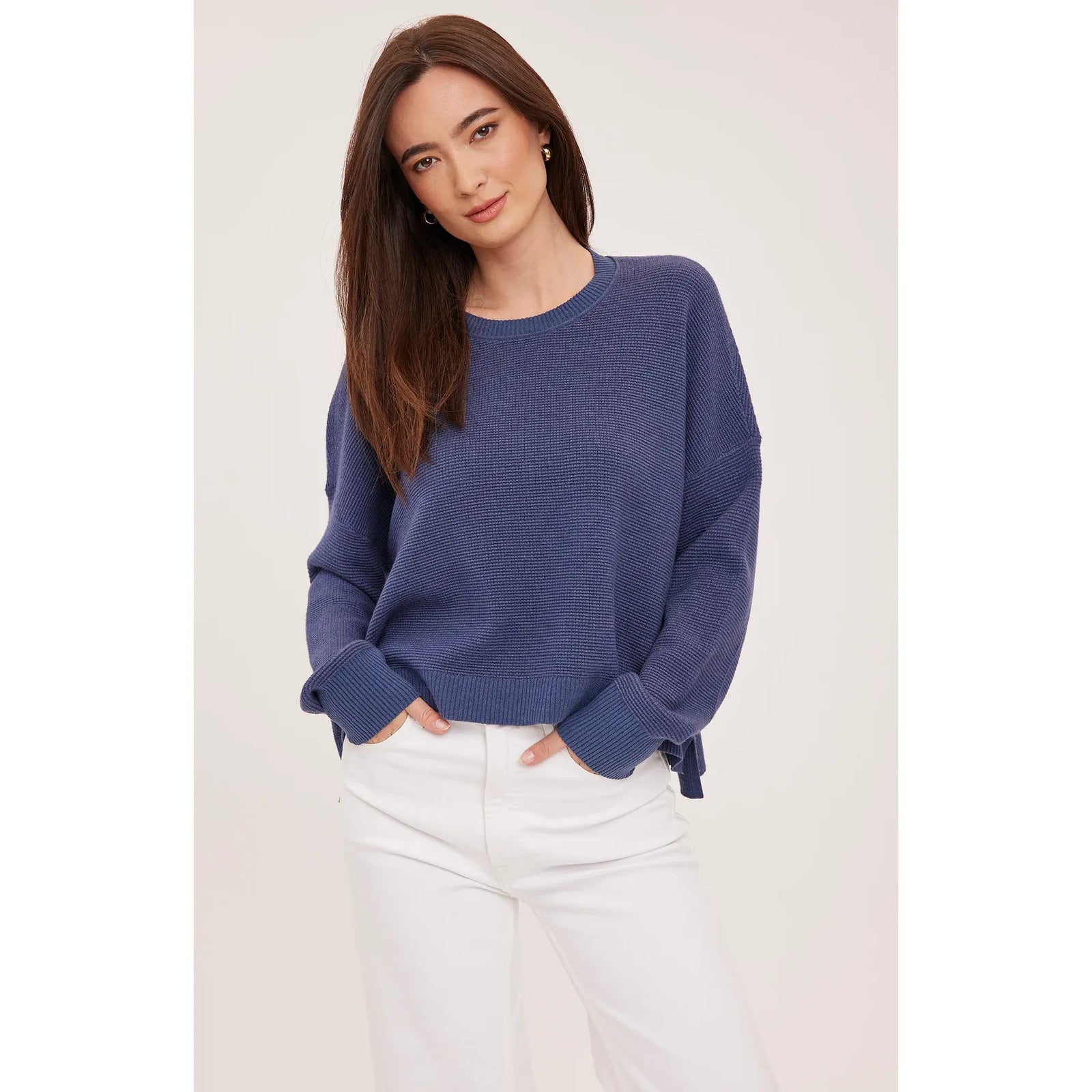 Blue waffle knit crewneck sweater with oversized fit and side slits, styled with white jeans.