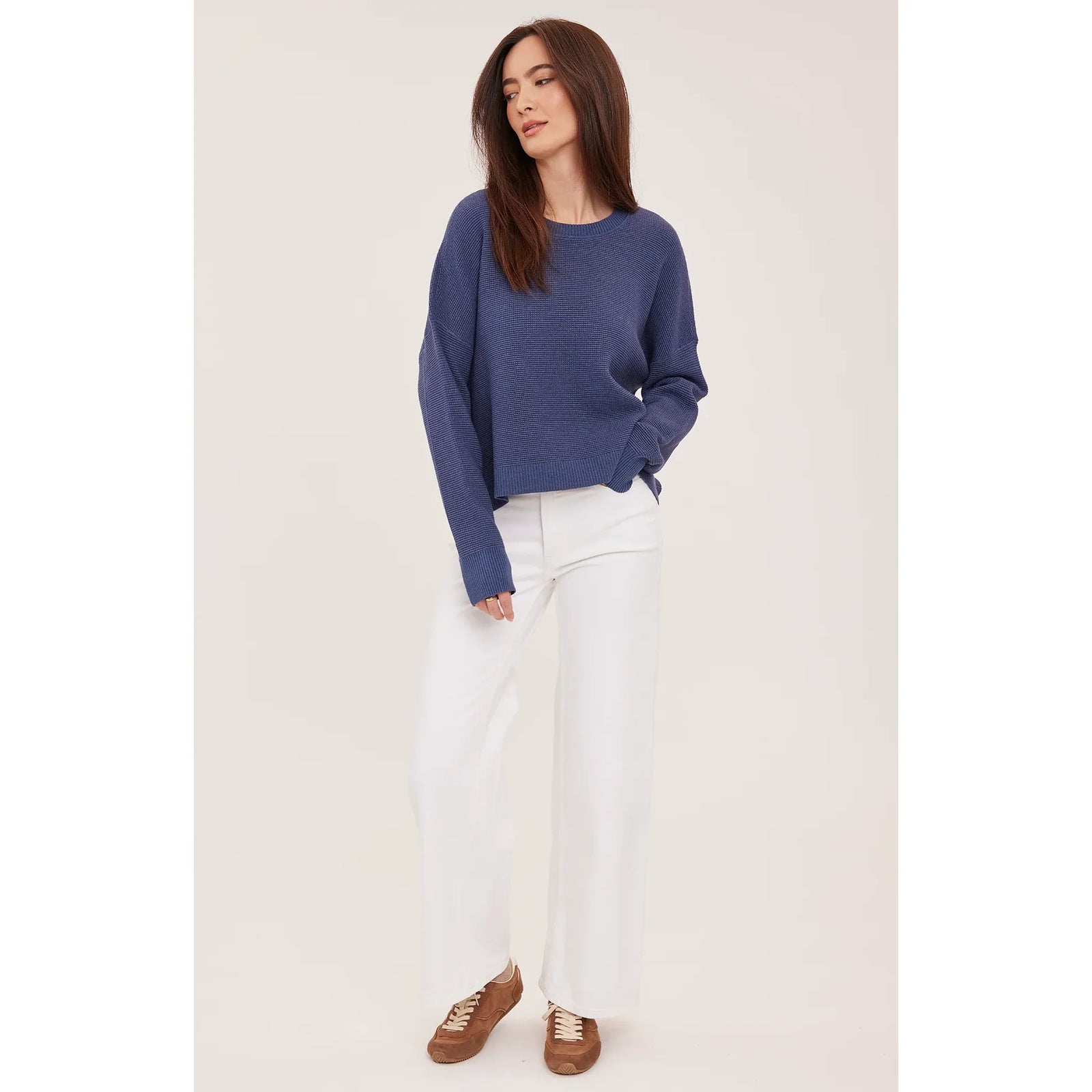 Blue waffle knit crewneck sweater with oversized fit and side slits, styled with white wide-leg pants and brown sneakers.