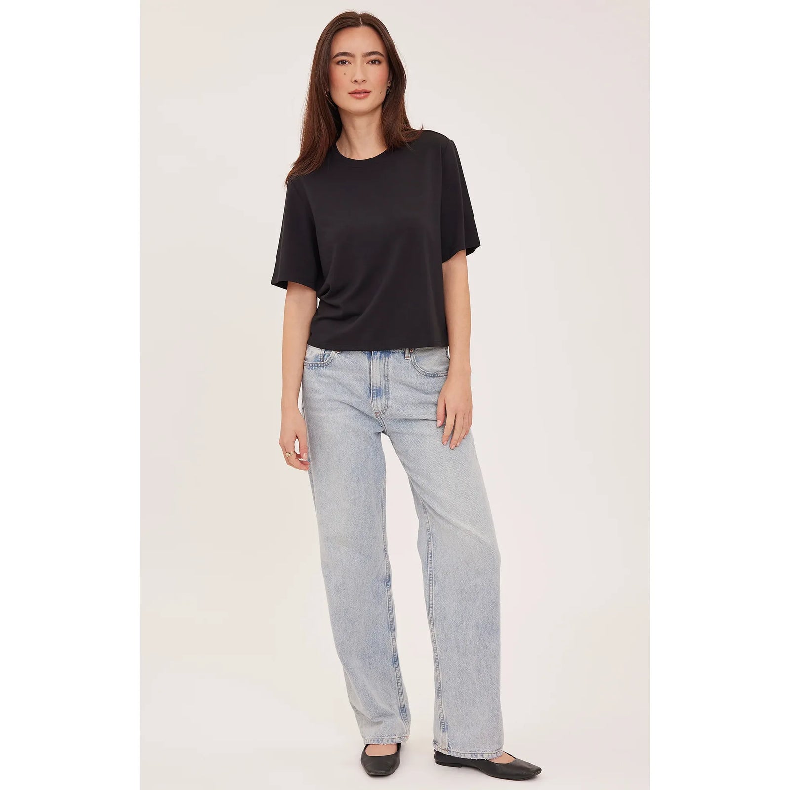 Model wears a relaxed fit black crew neck t-shirt with soft cotton-modal fabric, styled with light wash wide-leg jeans and flat shoes.