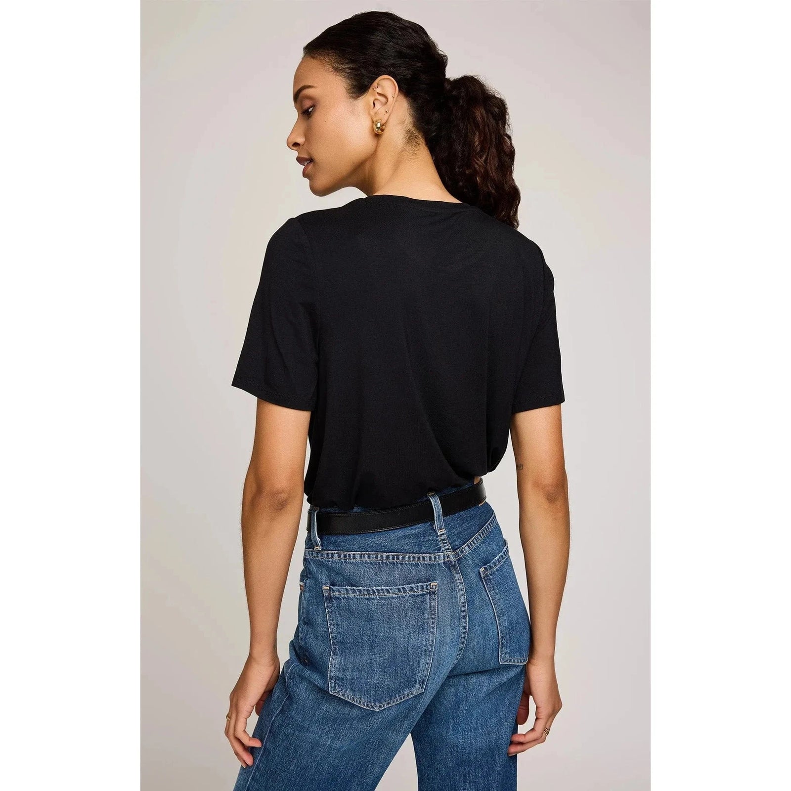 Back view of a model in a black Gentle Fawn Brielle TShirt with a relaxed fit, tucked into high-rise jeans.