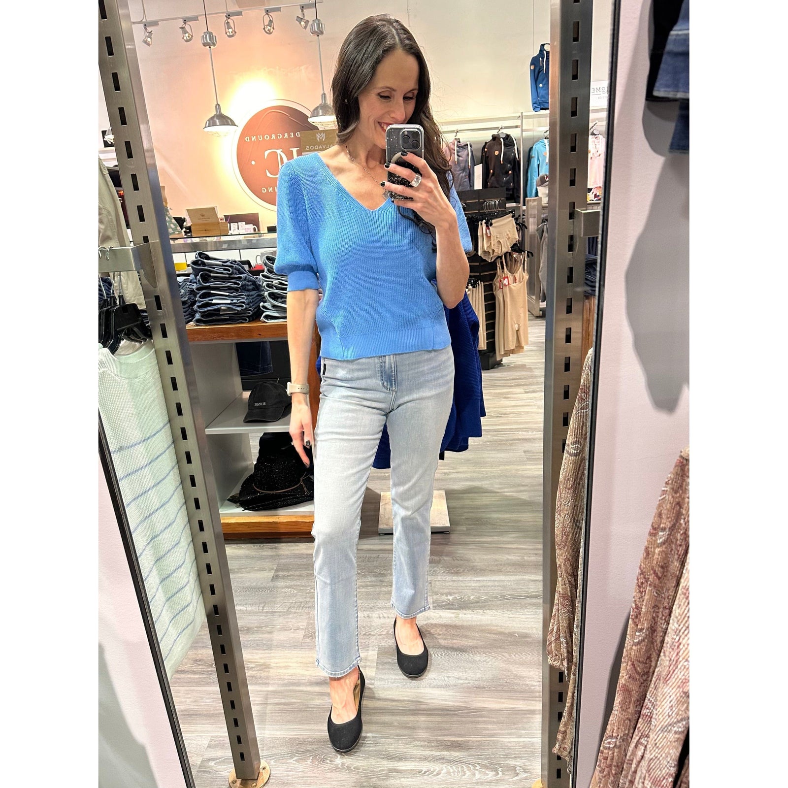 Gentle Fawn Phoebe V-Neck Sweater in blue with puff sleeves, worn by a shopper in a store.