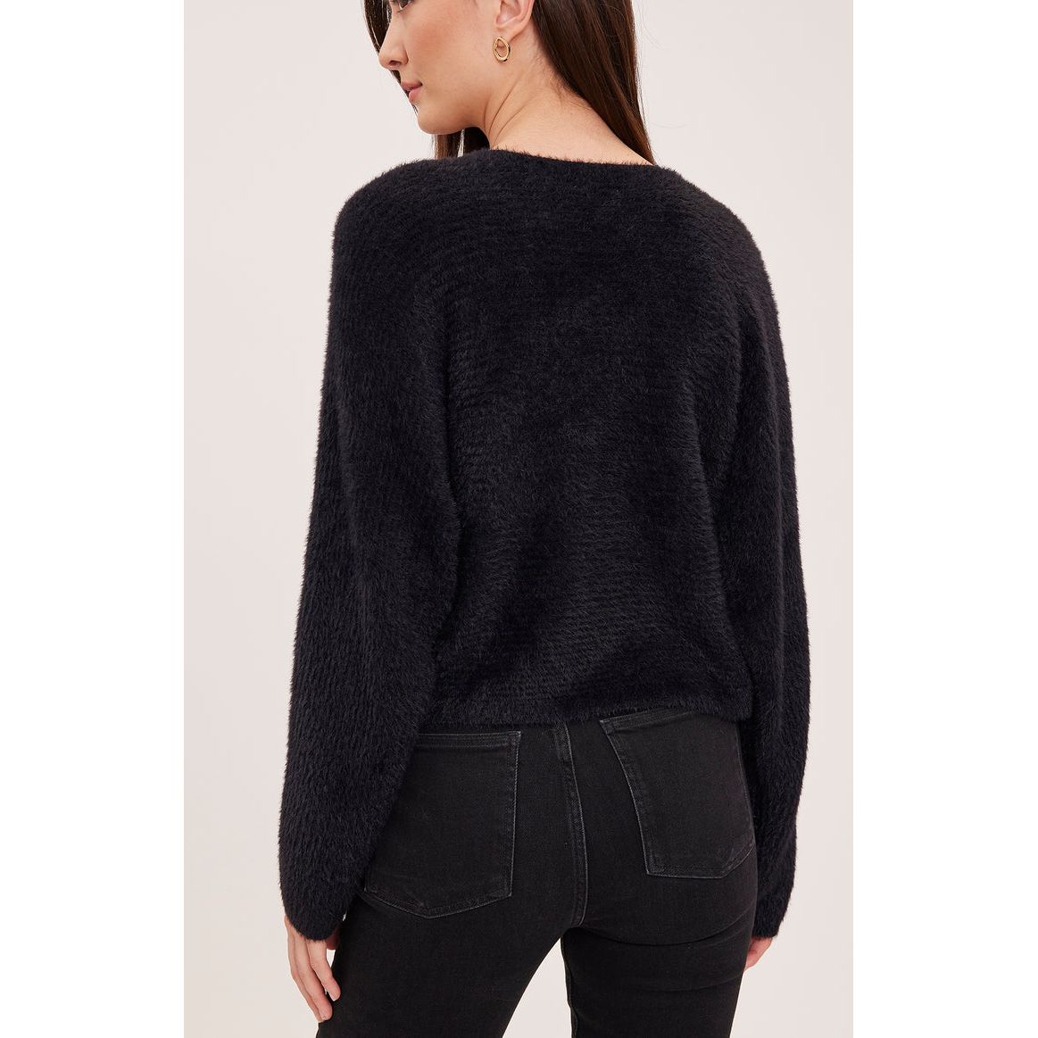 Back view of a plush, black chunky knit sweater with dolman sleeves paired with black denim jeans.