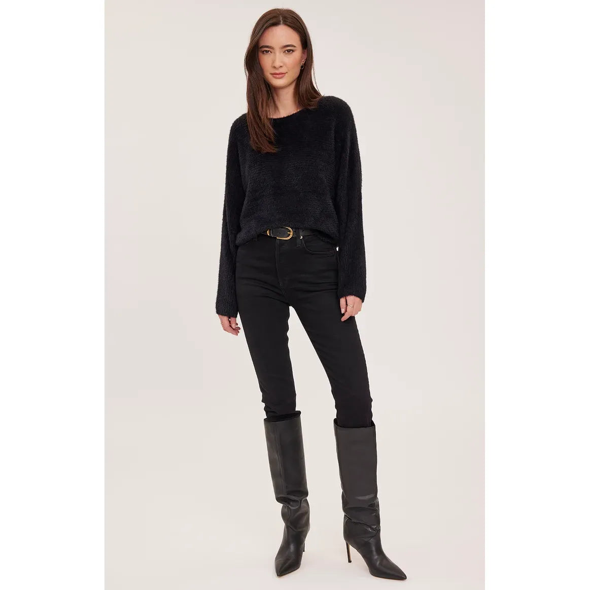 Model wearing a plush, black chunky knit sweater with dolman sleeves, styled with black jeans and tall boots for a relaxed fall look.
