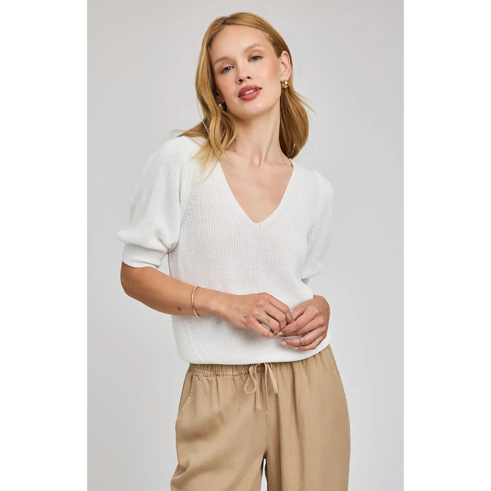 Gentle Fawn Phoebe V-Neck Sweater in white knit with puff sleeves, paired with beige pants.