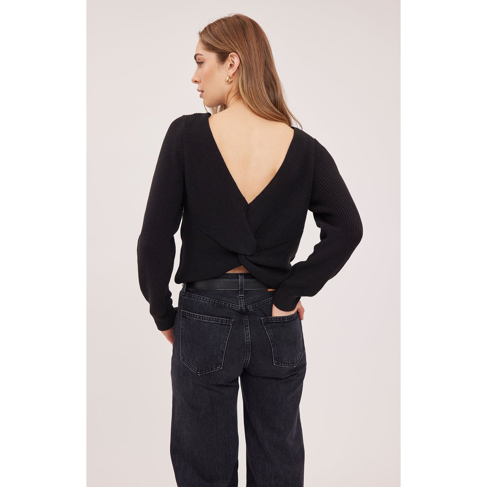 Back view of black Ramona sweater featuring a deep V-opening and twisted detail at the hem, paired with dark denim jeans.