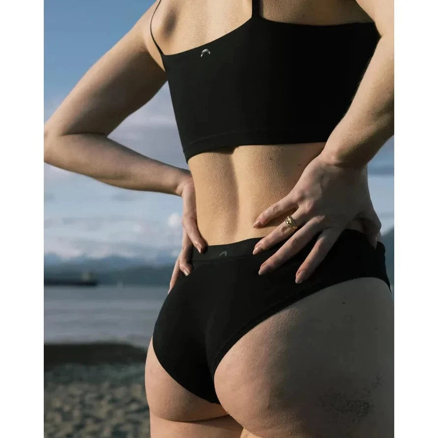 HuHa Cheeky Mineral Undies in black, model by the beach showing a flattering half-coverage.