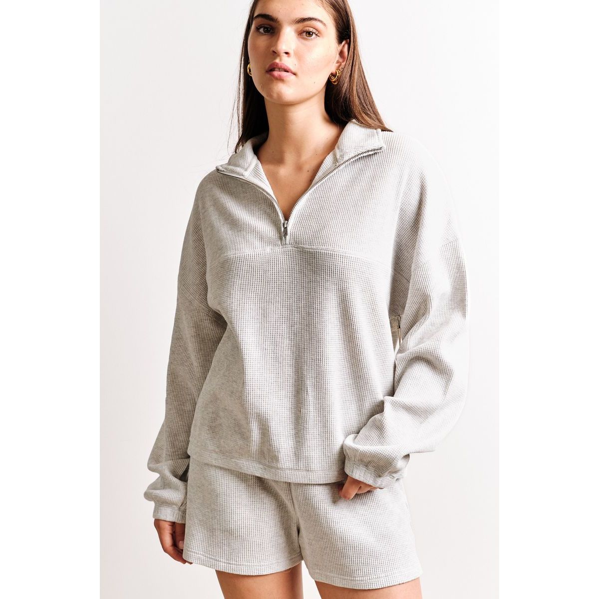 Kuwalla Bailey Waffle Zip Up long-sleeve top in light gray waffle knit with half-zip, model wearing matching shorts.