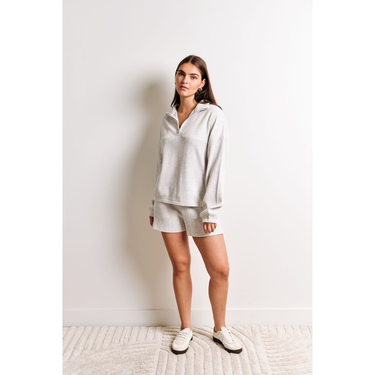 Model wearing Kuwalla Bailey Waffle Zip Up in light gray waffle knit, long-sleeve, half-zip, with matching shorts.