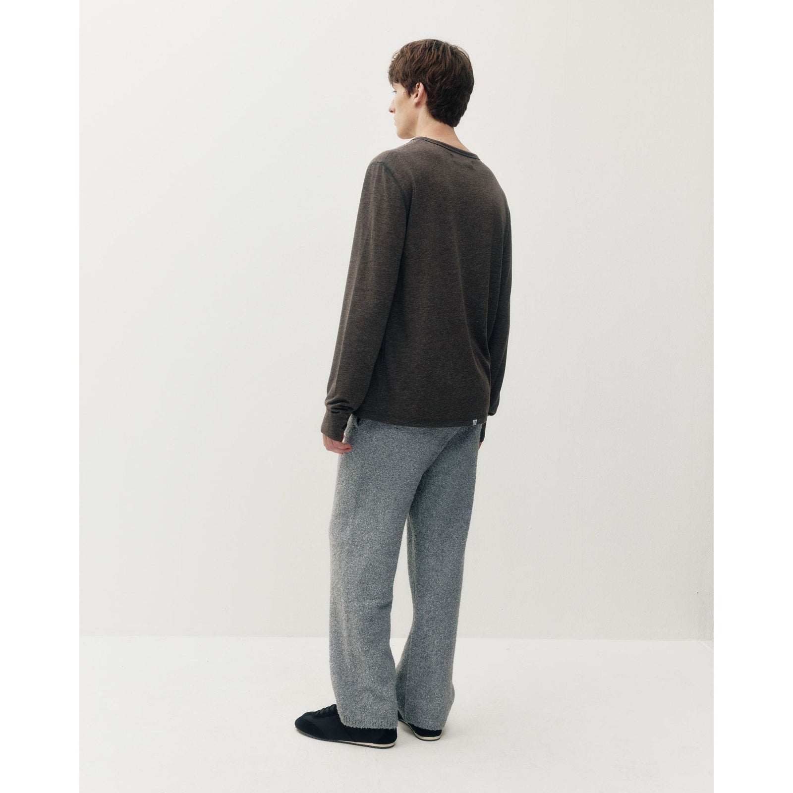 Back view of a man wearing a dark heathered thermal long sleeve tee and grey textured pants against a white background.