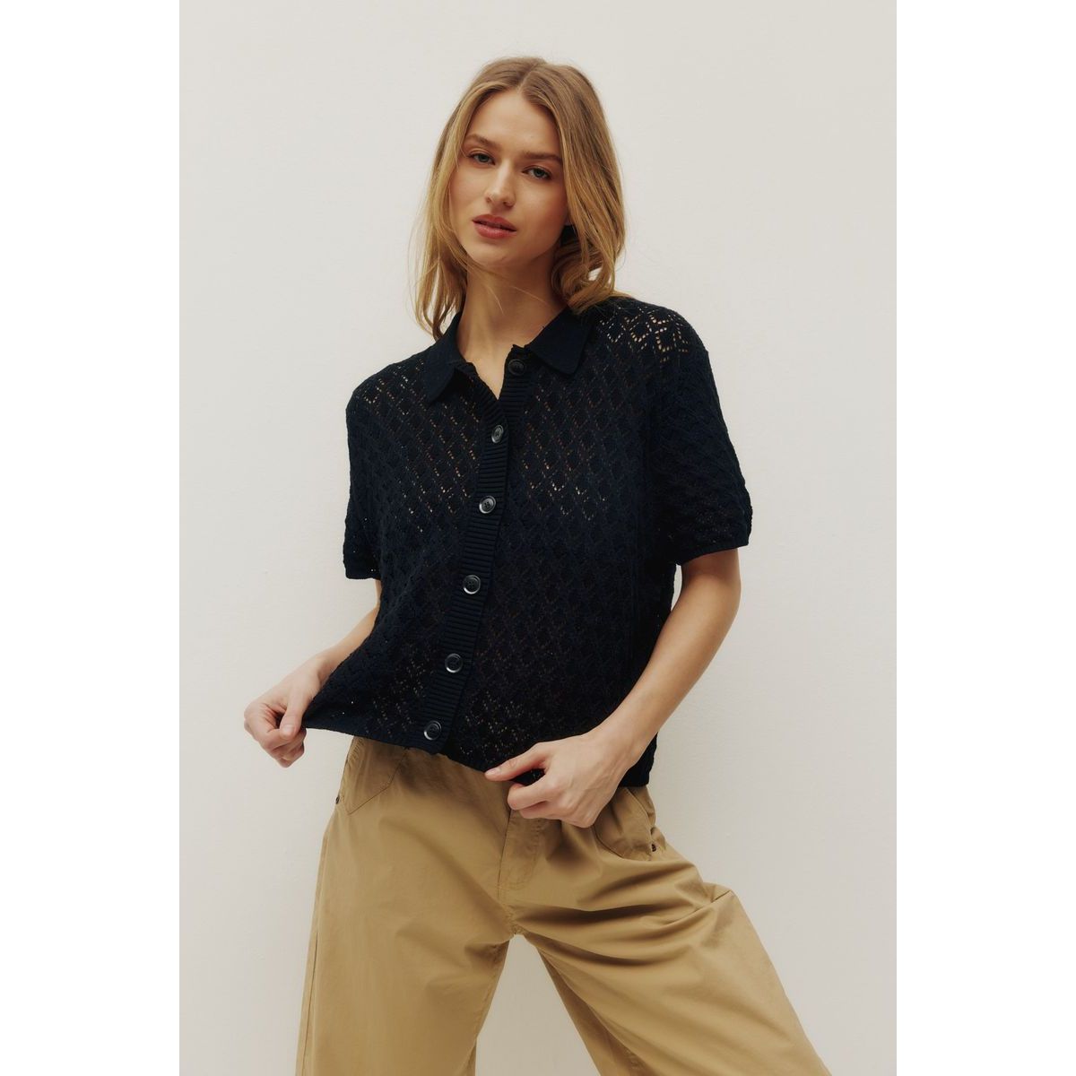 Kuwalla Monica Beach Knit Button Up black lace-knit short-sleeve top worn by a model in beige pants.