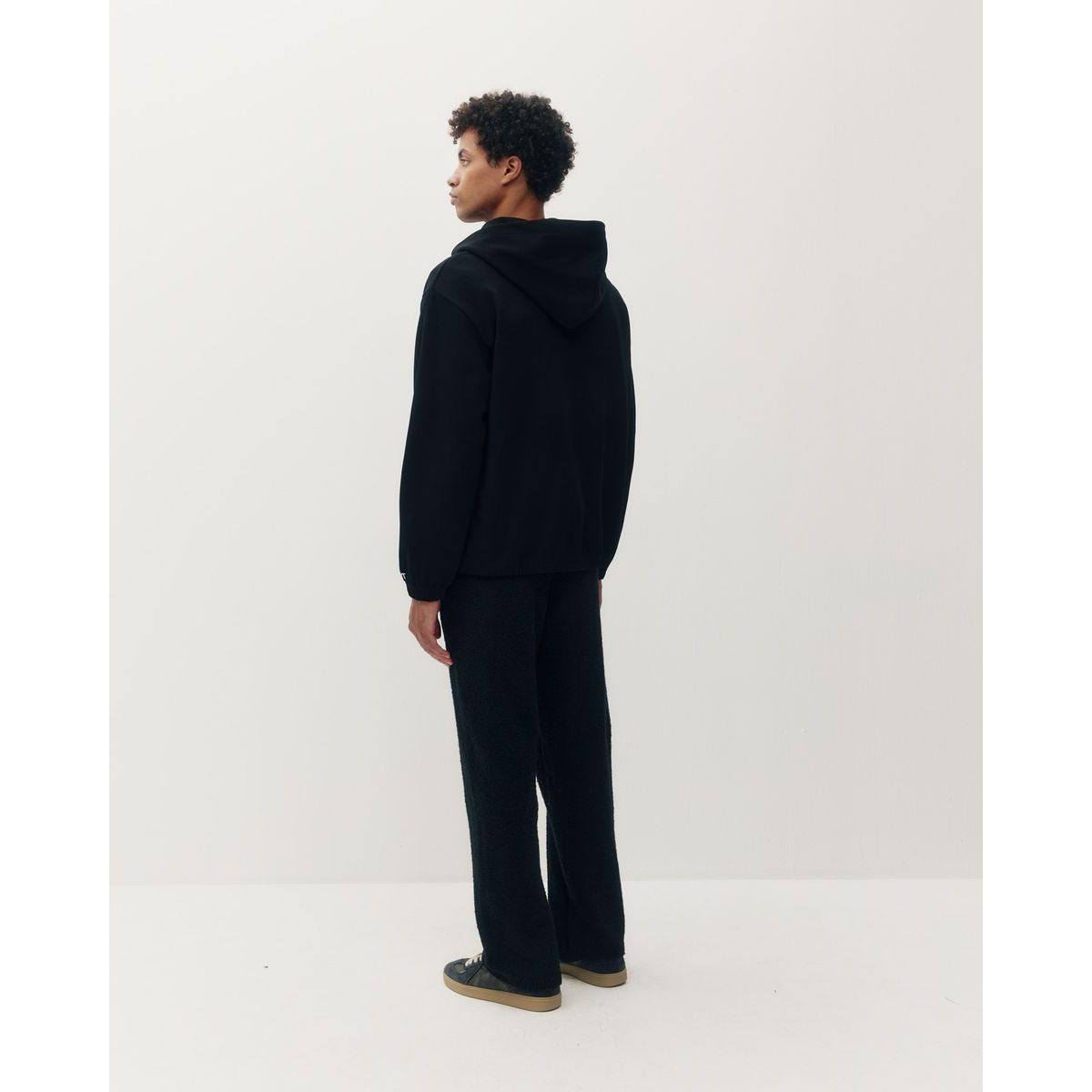 Back view of a black ribbed zip hoodie worn by a model with matching black textured trousers against a white background.