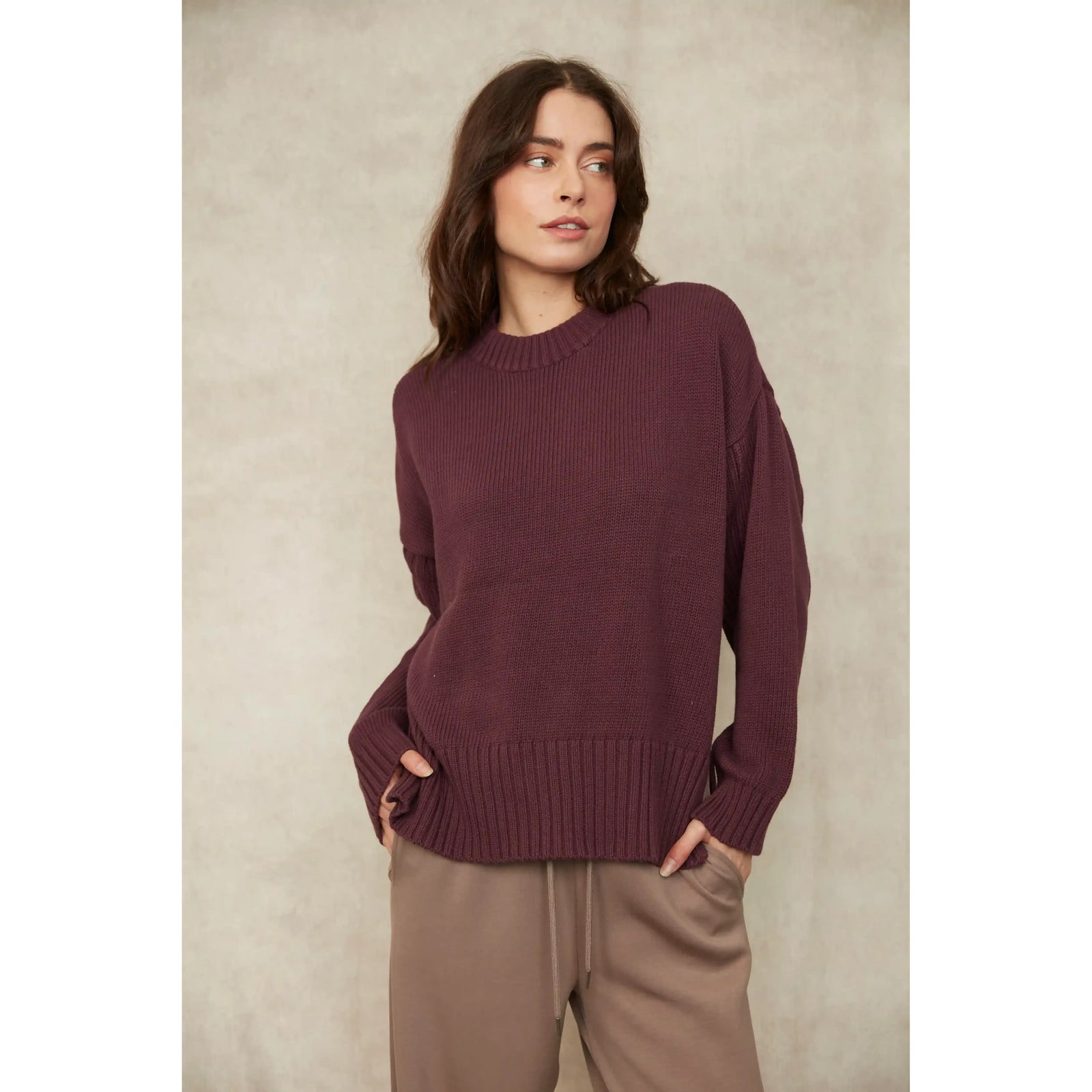 Woman wearing a burgundy long sleeve crew neck cotton knit pullover with ribbed trim at the hem and cuffs.
