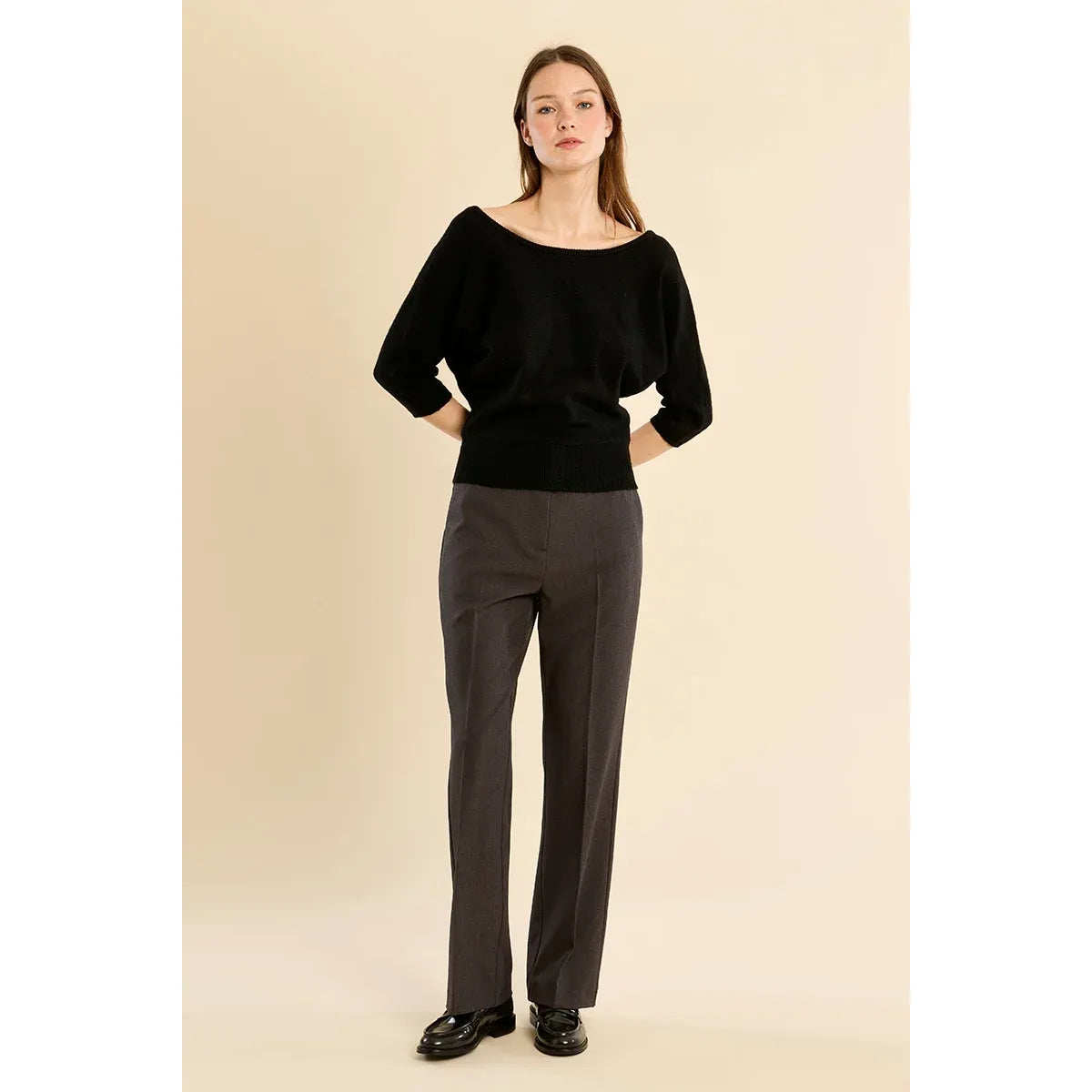 Black open-back 3/4 sleeve knit sweater with boat neckline, wide fit, and ribbed hem paired with grey trousers.
