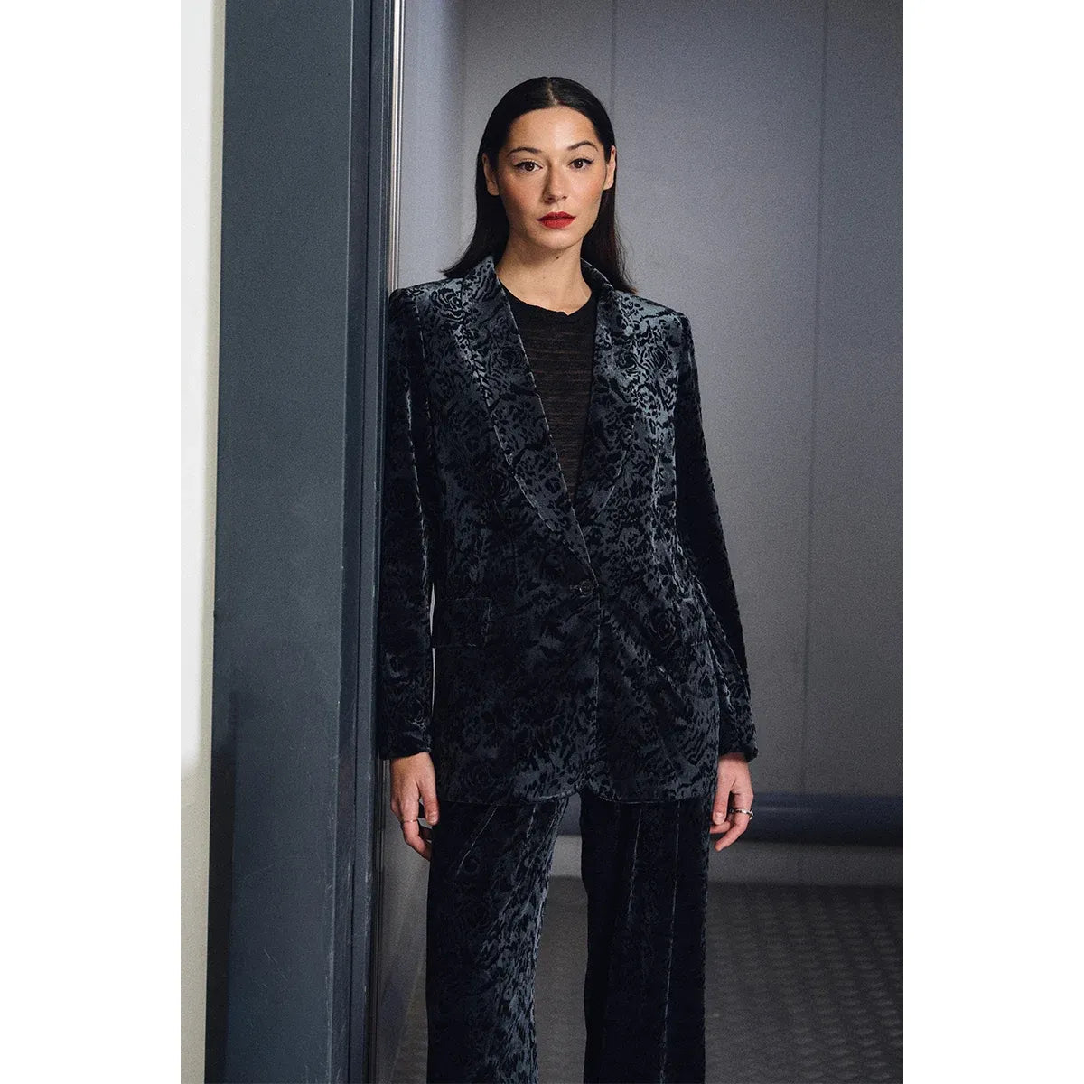 Dark floral velvet blazer with V-neck and single button closure, styled over a black top with matching trousers.