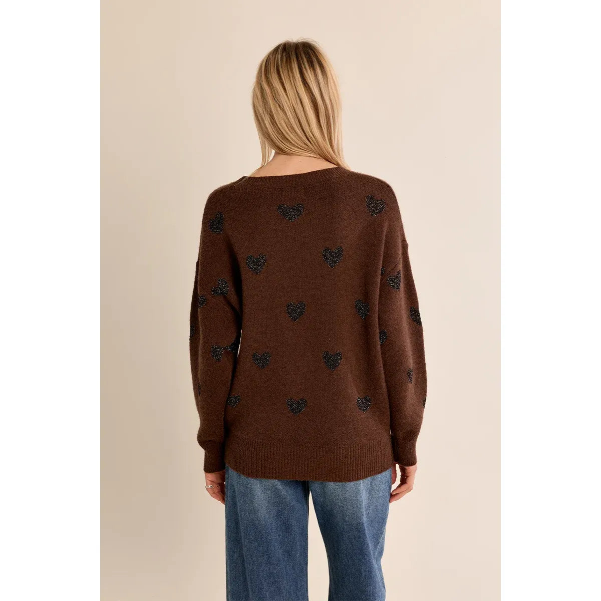 Back view of a brown knit sweater with glittery black heart pattern, round neckline, and relaxed fit over blue jeans.