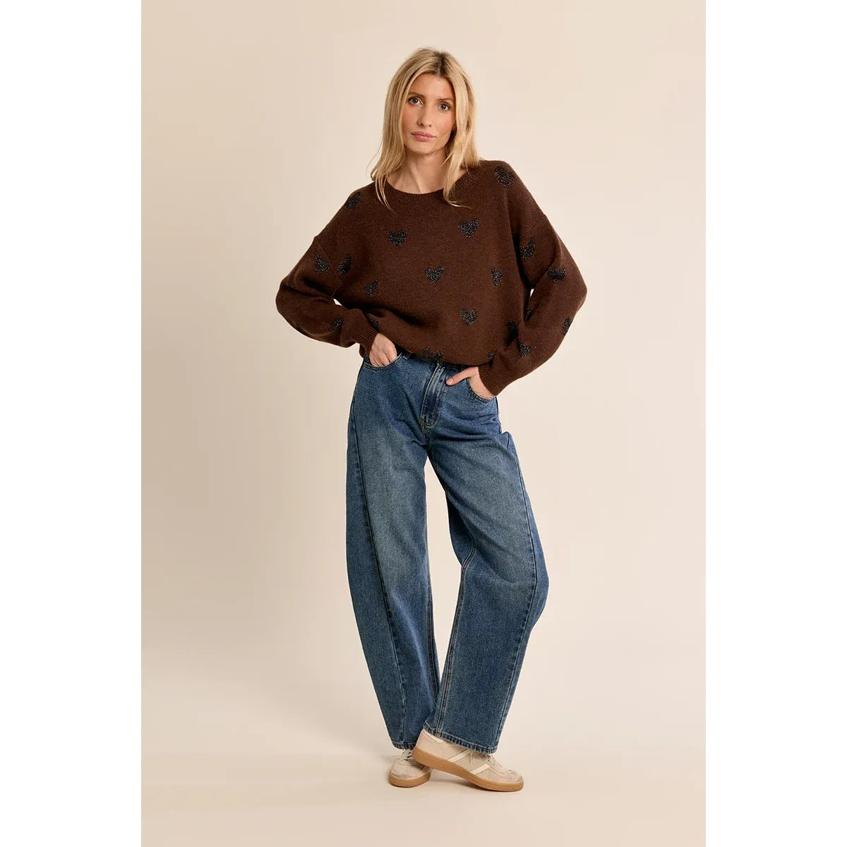 Brown knit sweater with glittery heart pattern, round neckline, and relaxed fit paired with blue jeans.