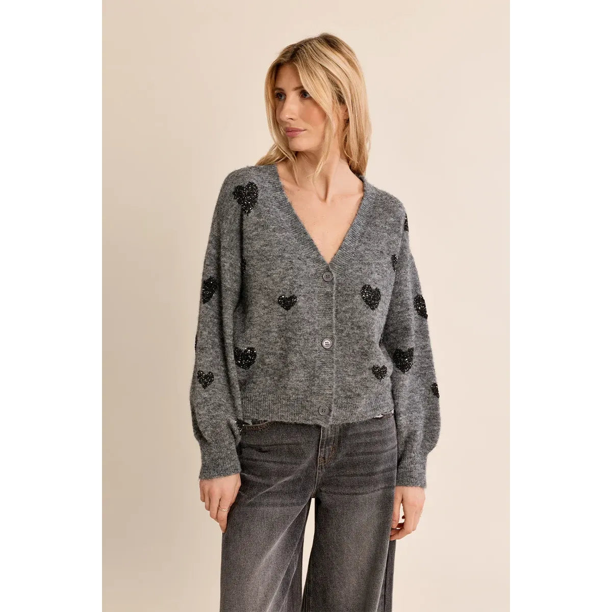 Grey knit cardigan with black sequin hearts, balloon sleeves, and V-neck paired with dark jeans for a cozy fall look.