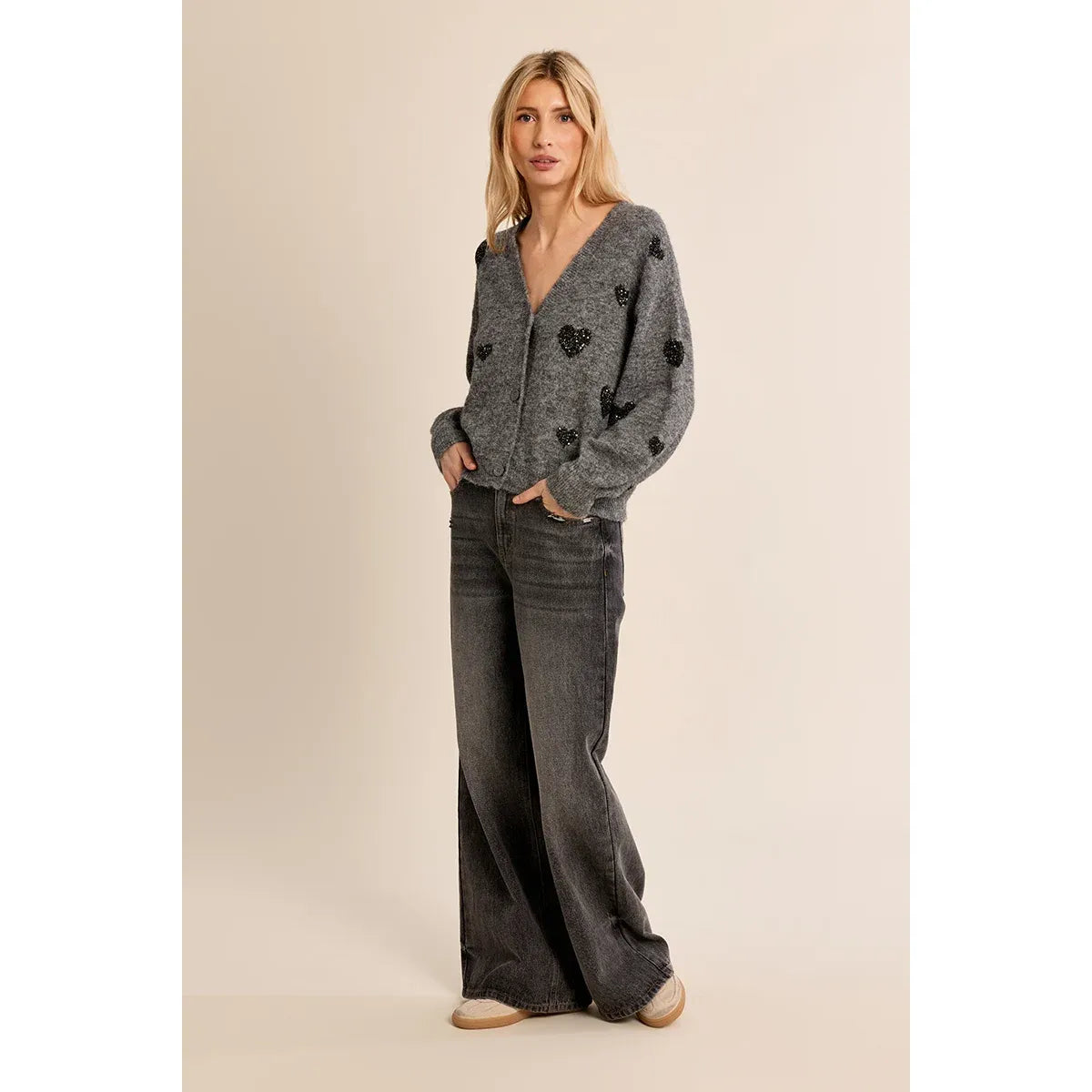 Grey knit cardigan with black heart pattern, balloon sleeves, and V-neck paired with dark denim jeans for a fall look.