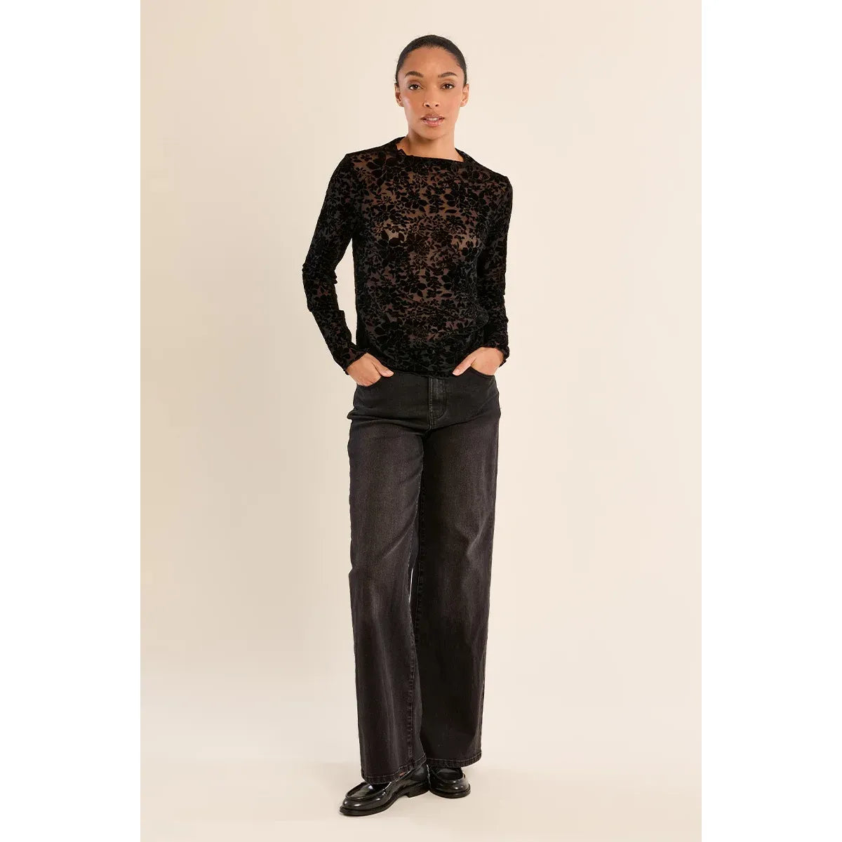 Black semi-sheer lace mock neck top with long sleeves, styled with dark wide-leg jeans and black loafers.