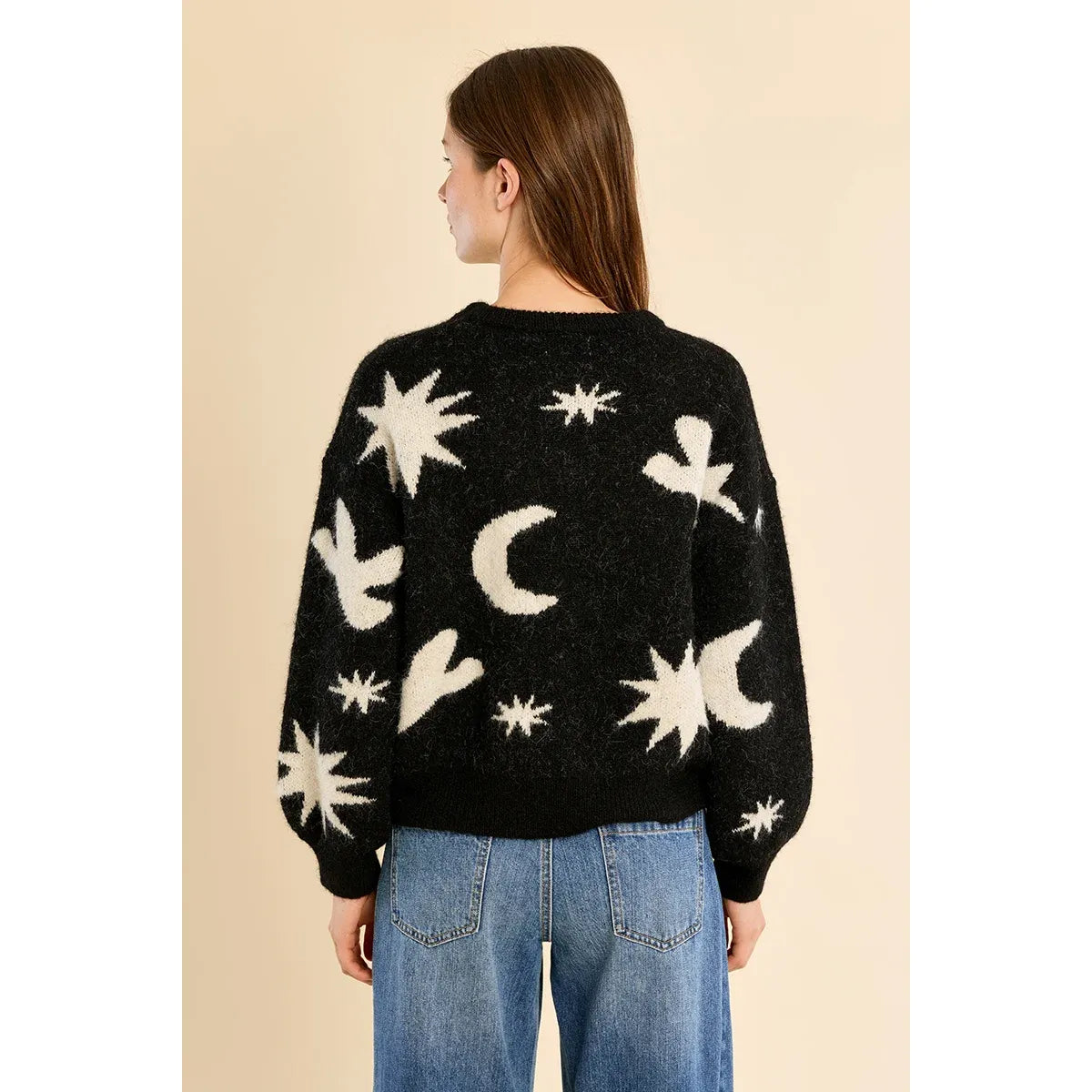 Back view of a fuzzy black knit sweater with white stars, moons, and birds, featuring balloon sleeves worn with blue jeans.