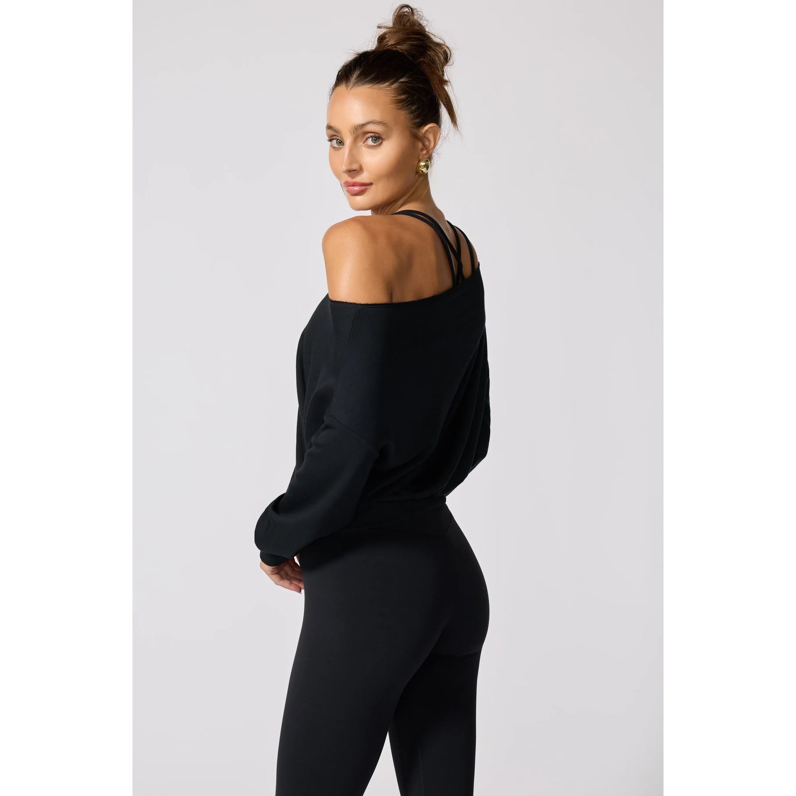 Black off-the-shoulder sweatshirt featuring raw edge neckline detailing, ribbed cuffs, and a relaxed fit paired with black leggings.