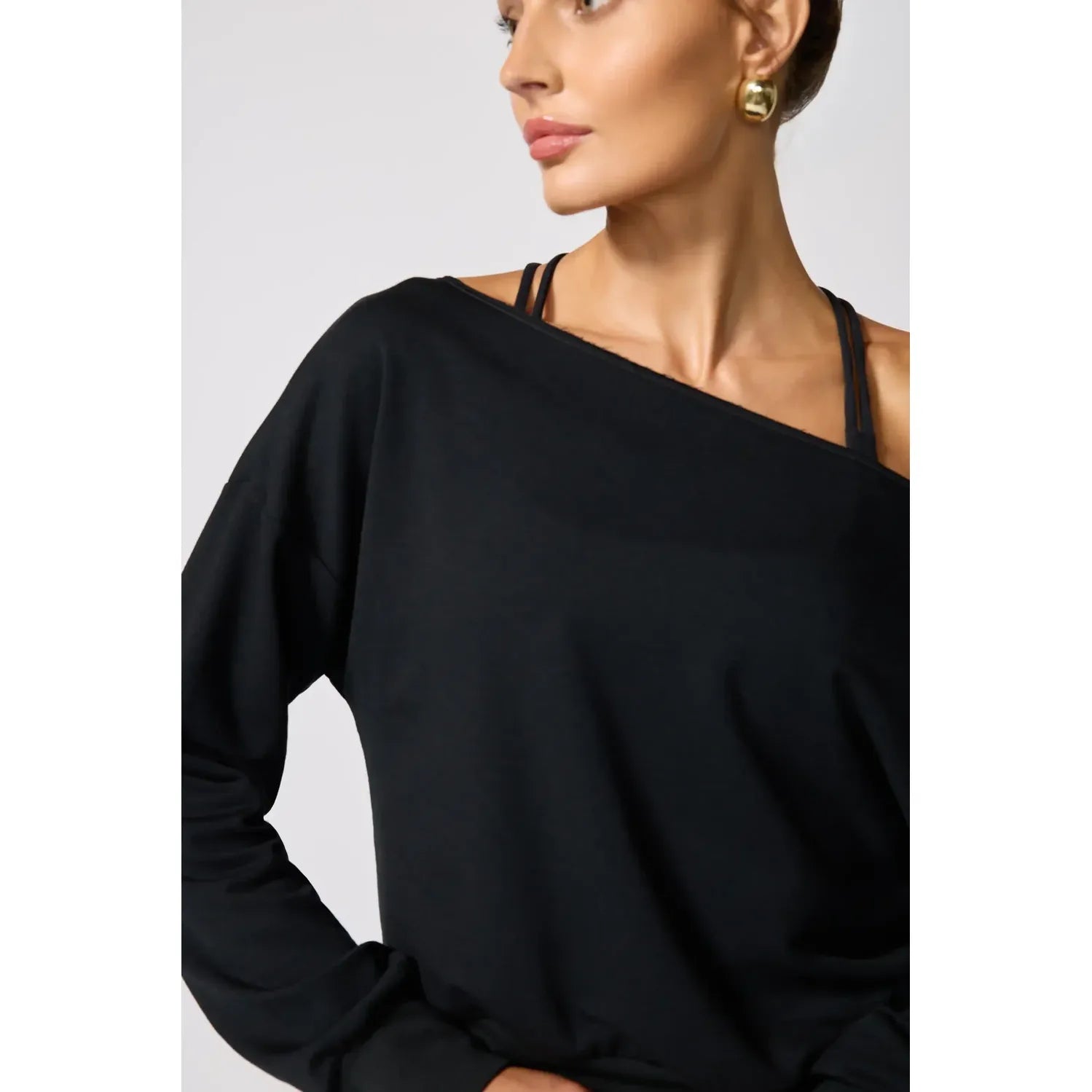 Black flashdance sweatshirt featuring an off-shoulder neckline with raw edge detailing, layered over a strap top for modern casual style.