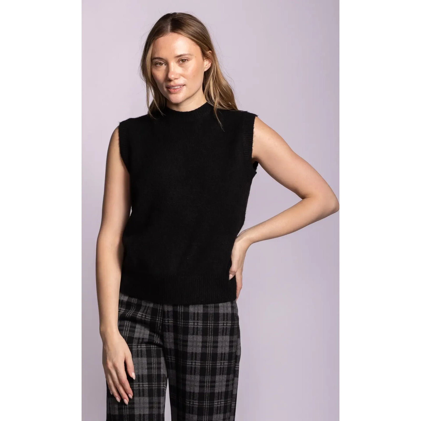 Black sleeveless ribbed sweater with structured shoulders and hem, styled as a layering essential with plaid trousers.