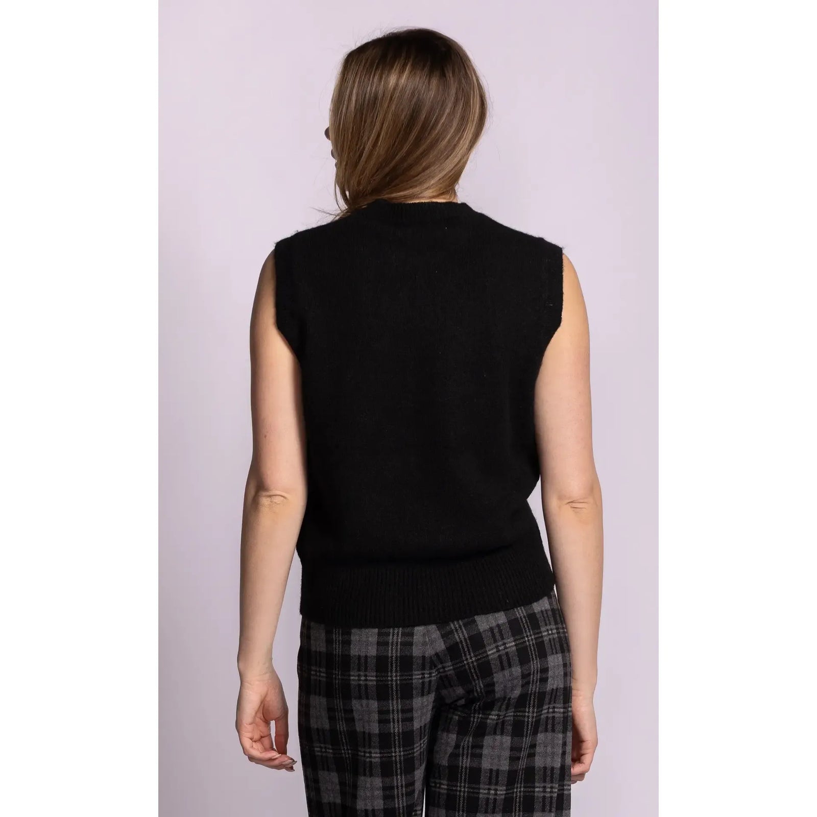 Back view of a black sleeveless ribbed sweater with structured shoulders and hem, styled with plaid pants.