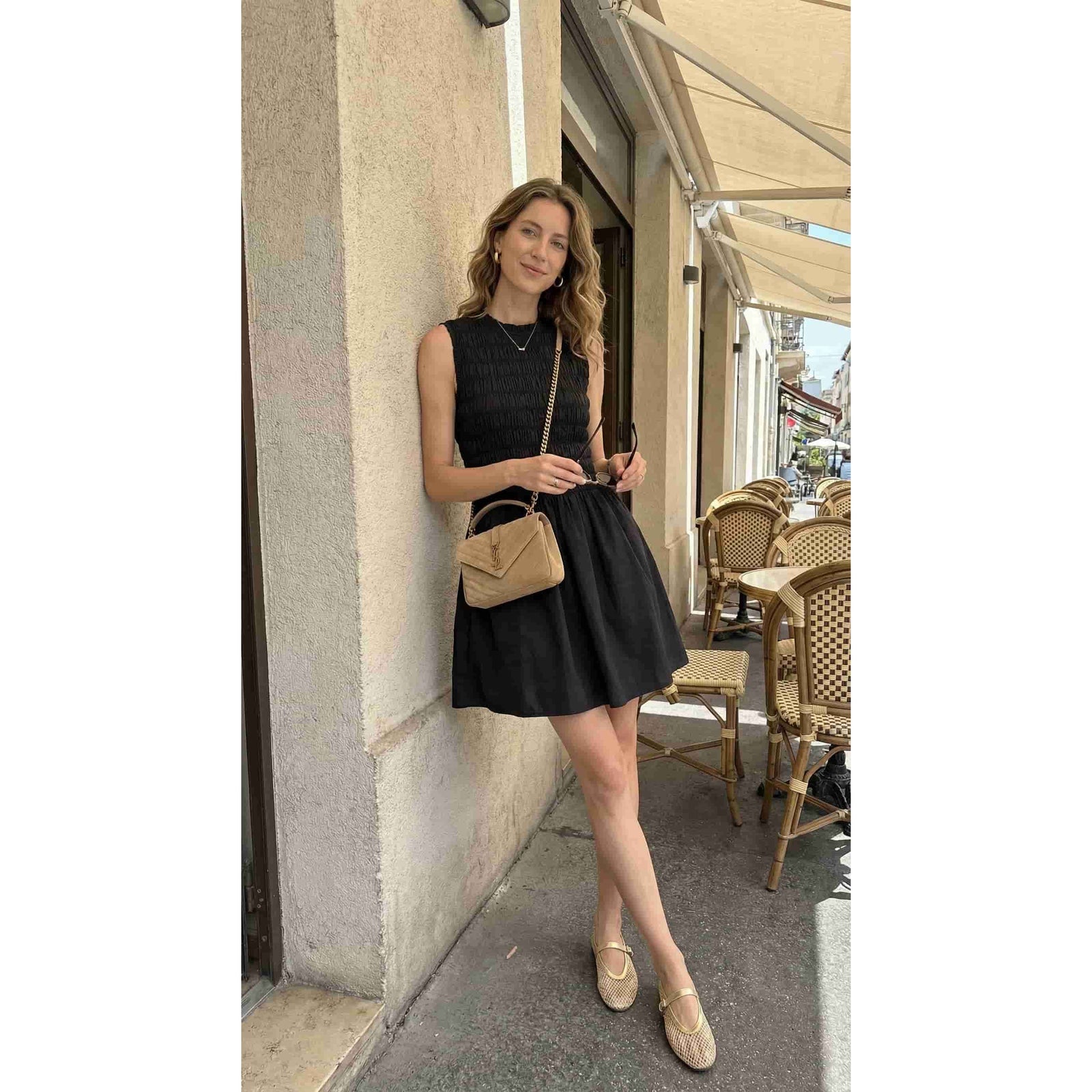 Woman in Priv PrimRuched Cocktail Dress, black ruched bodice with flowy skirt and beige crossbody bag at a cafe.
