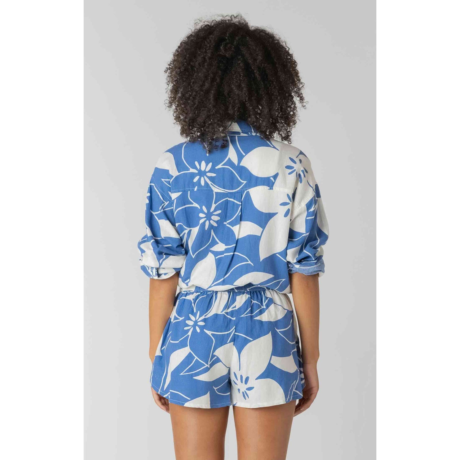 Back view of model in Room 34 Button Front Linen Shirt with blue floral print and matching shorts.