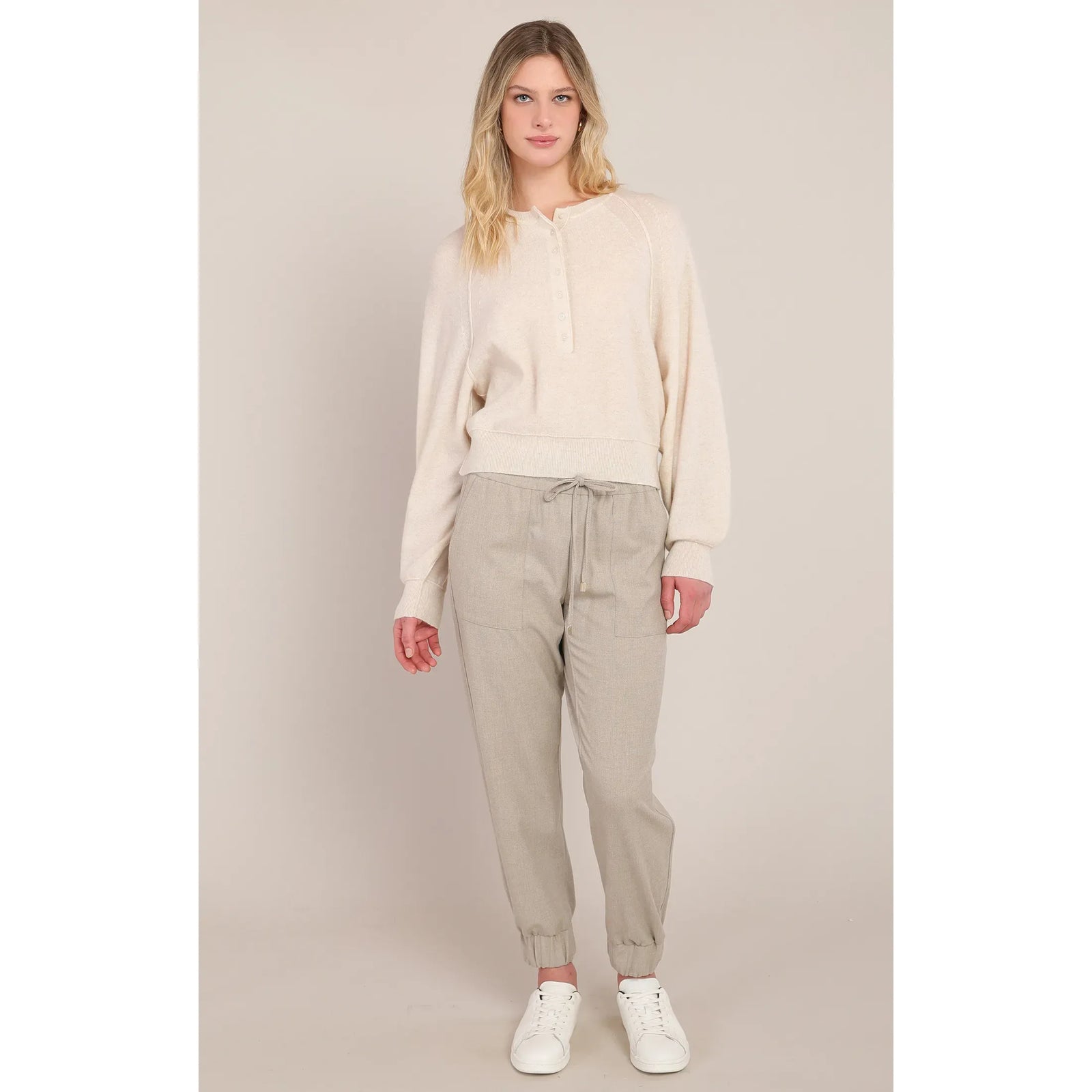 Model wearing beige cuffed hem pants with a drawstring waist and relaxed fit, styled with a cream sweater and white sneakers.