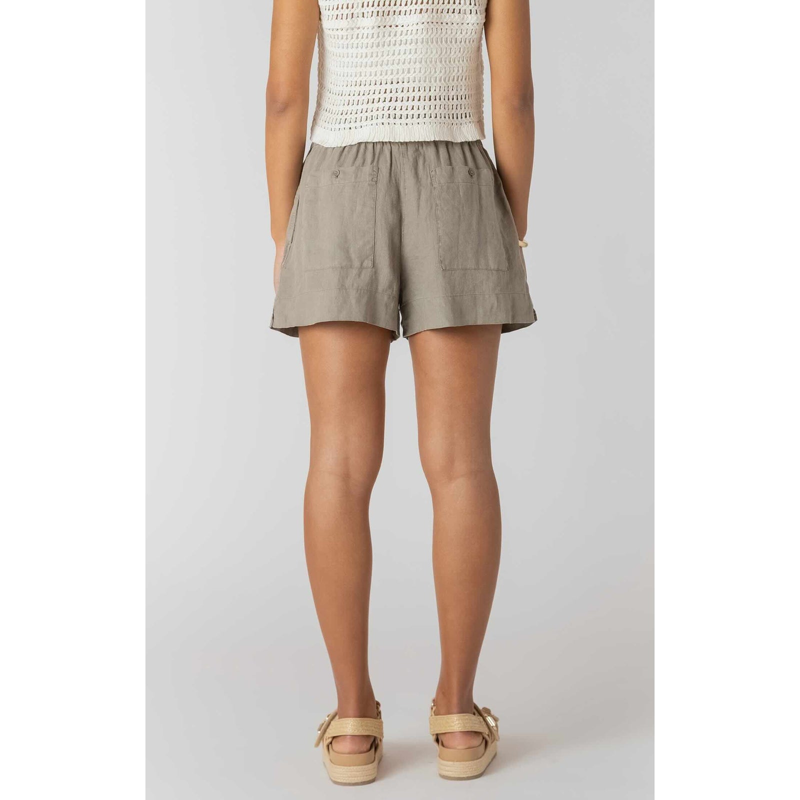 Back view of model wearing Room 34 Mid-rise Shorts in taupe, woven fabric with two back pockets.