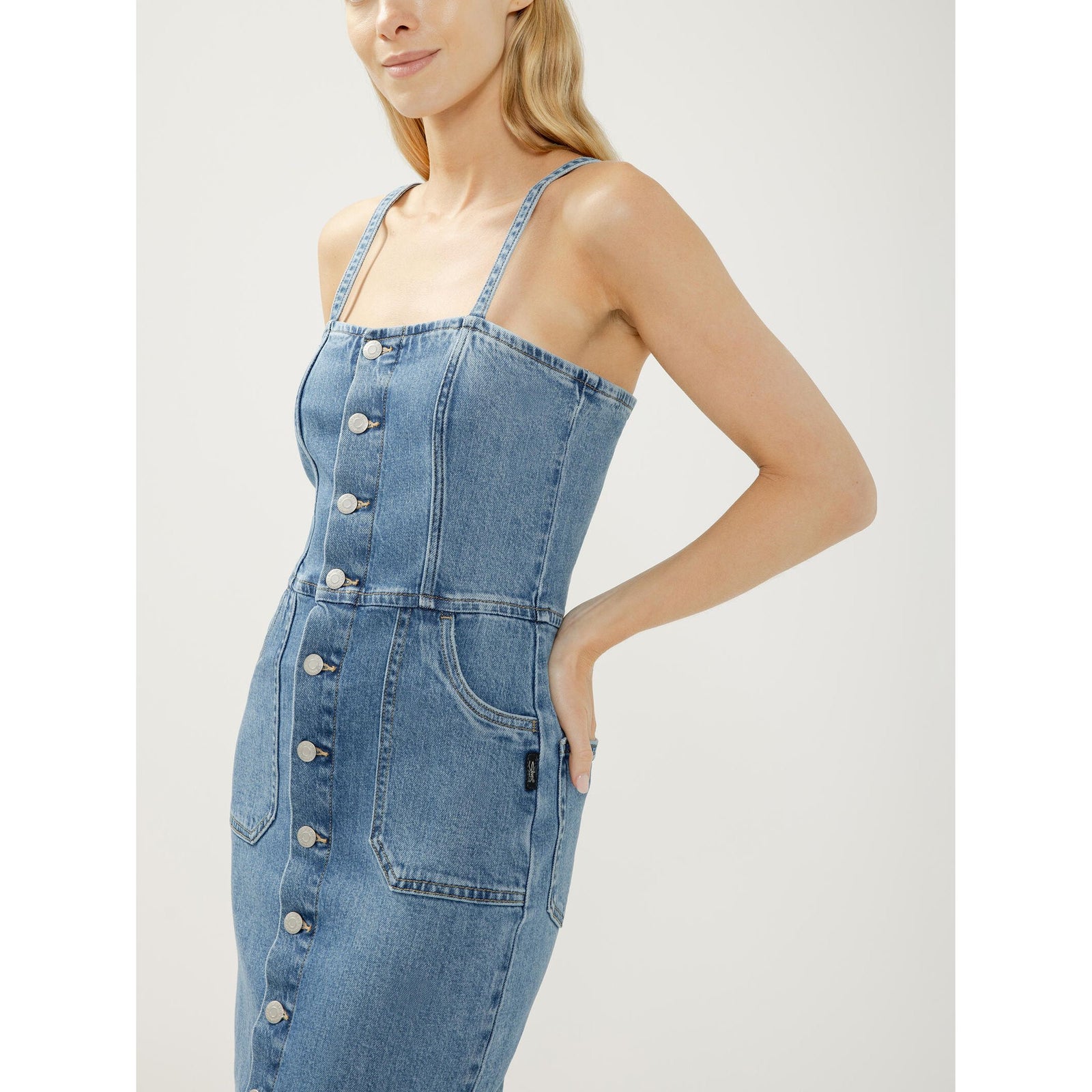 Denim midi dress with silver button-front closure, fitted silhouette, adjustable spaghetti straps, and front pockets.