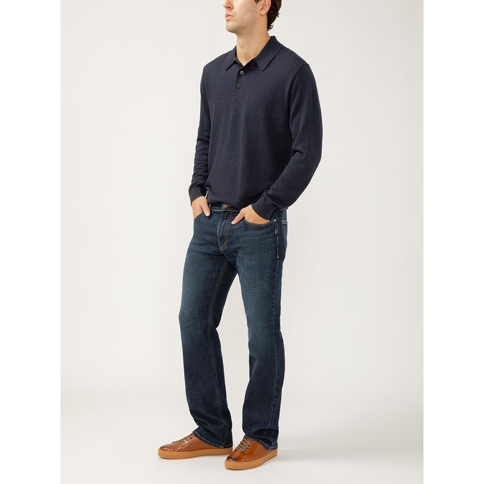 Silver Jace Slim Bootcut Luxe in Swing jeans on a man in a navy knit top with tan sneakers.
