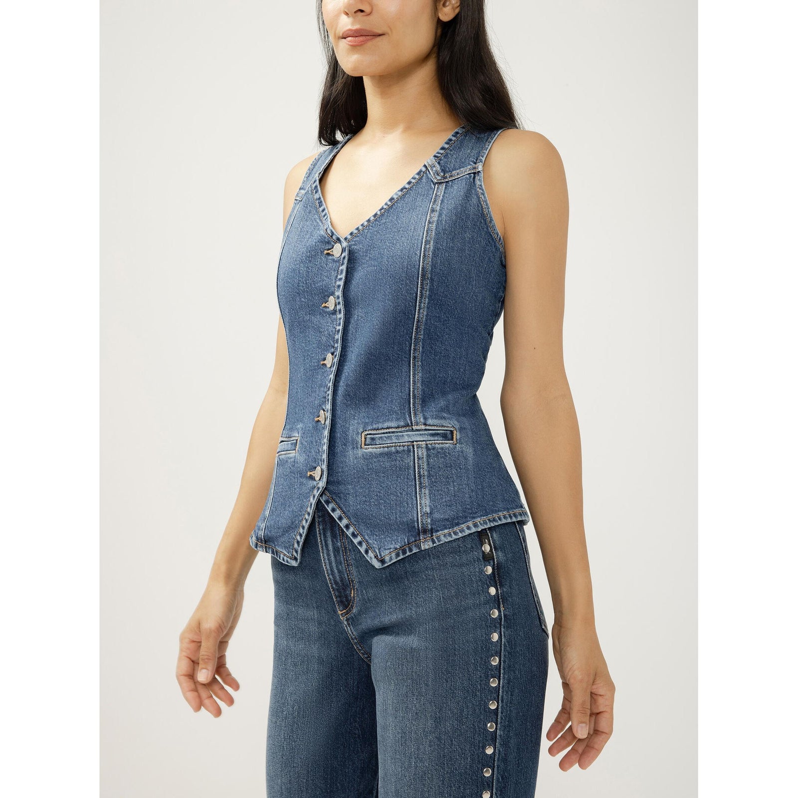 Blue longline denim vest with V-neck, button-front closure, functional front welt pockets, and a pointed hem.